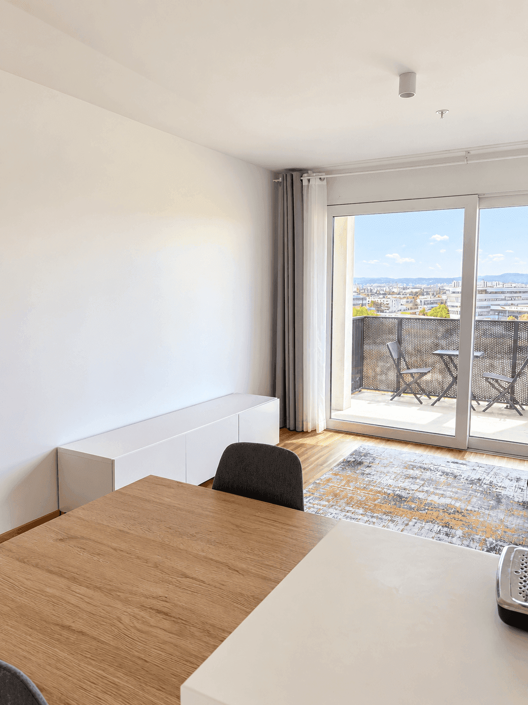 Offener Wohn-Essbereich mit Holztisch, modernem Sideboard und Zugang zum Balkon.