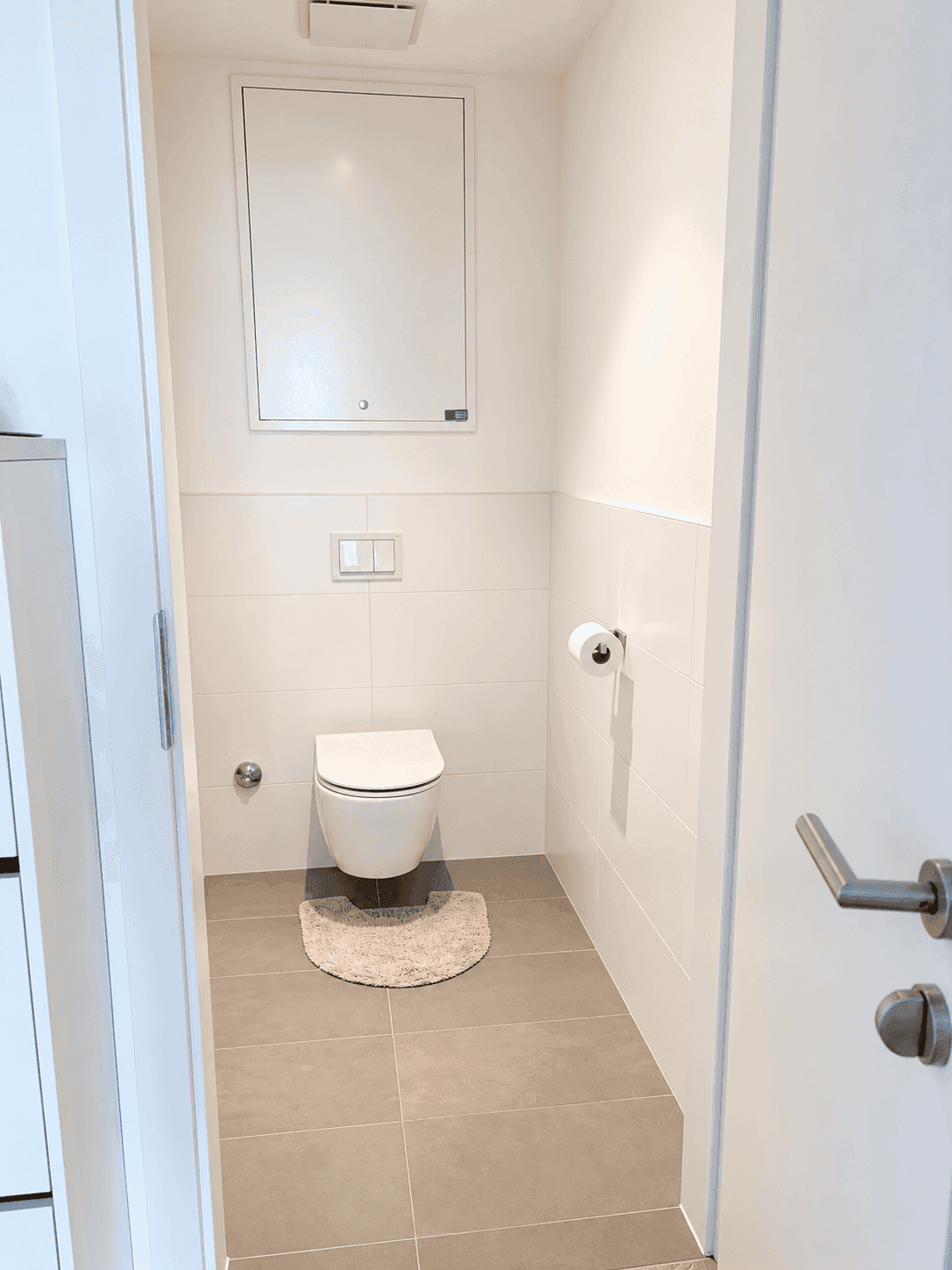 Kleines, modernes WC mit wandhängender Toilette und grauen Bodenfliesen.