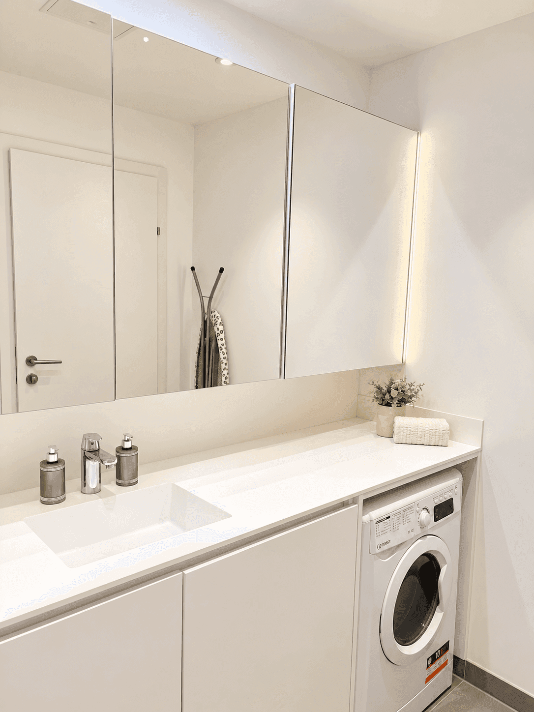 Modernes Badezimmer mit weißem Waschtisch, Spiegelschrank und integrierter Waschmaschine.