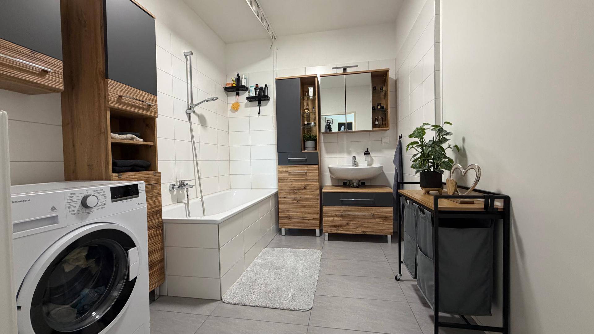 Modernes Badezimmer mit Badewanne, Waschbecken, Spiegelschrank und Waschmaschine.