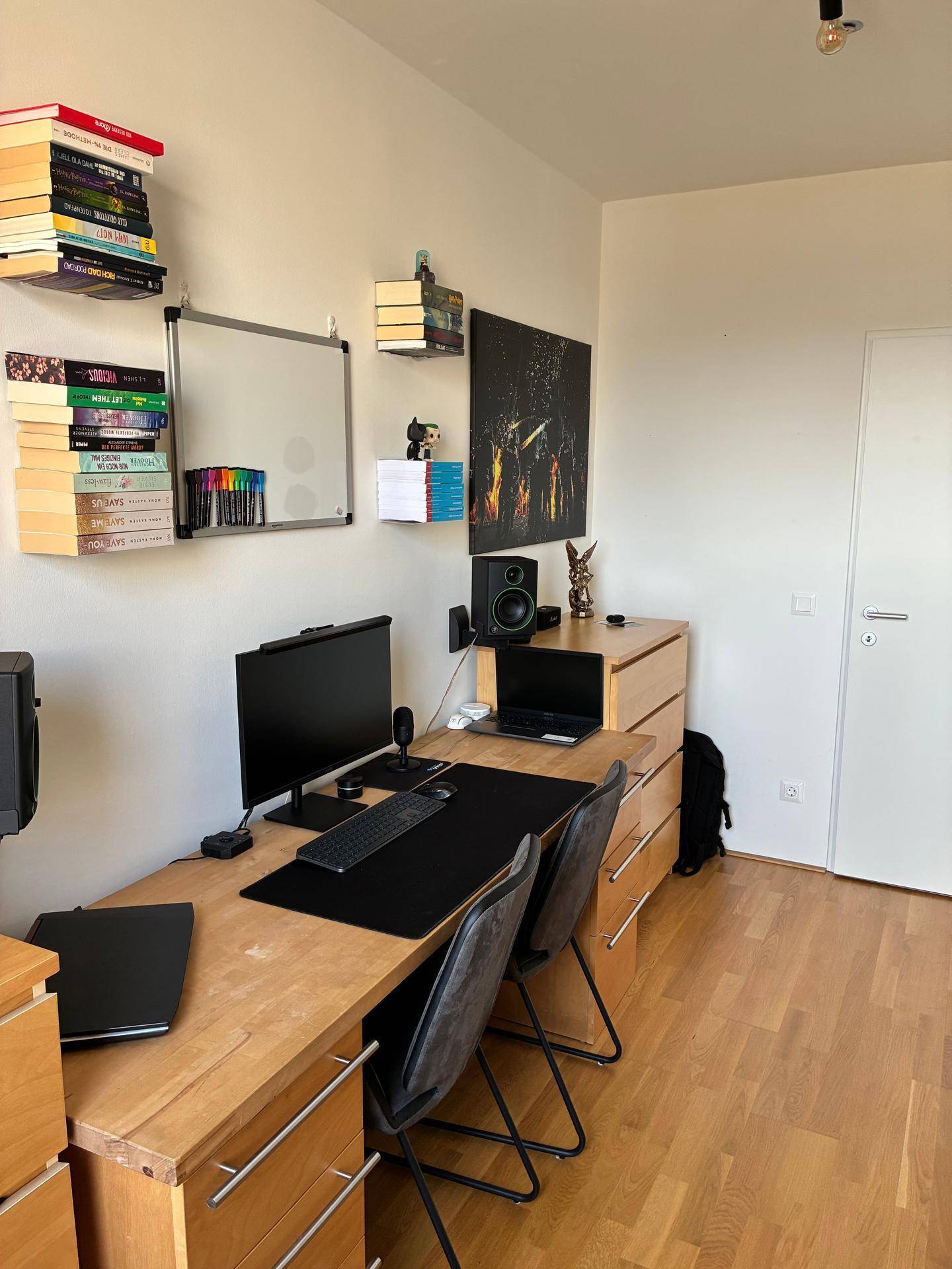 Arbeitsplatz mit Holzschreibtisch, Büchern und technischer Ausstattung in einem hellen Raum.