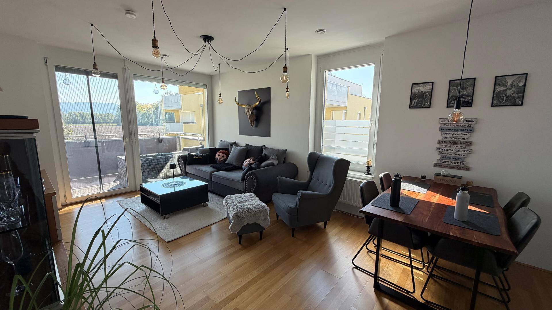 Offener Wohn-Essbereich mit Holzboden, gemütlichem Sofa und Zugang zu einem Balkon.