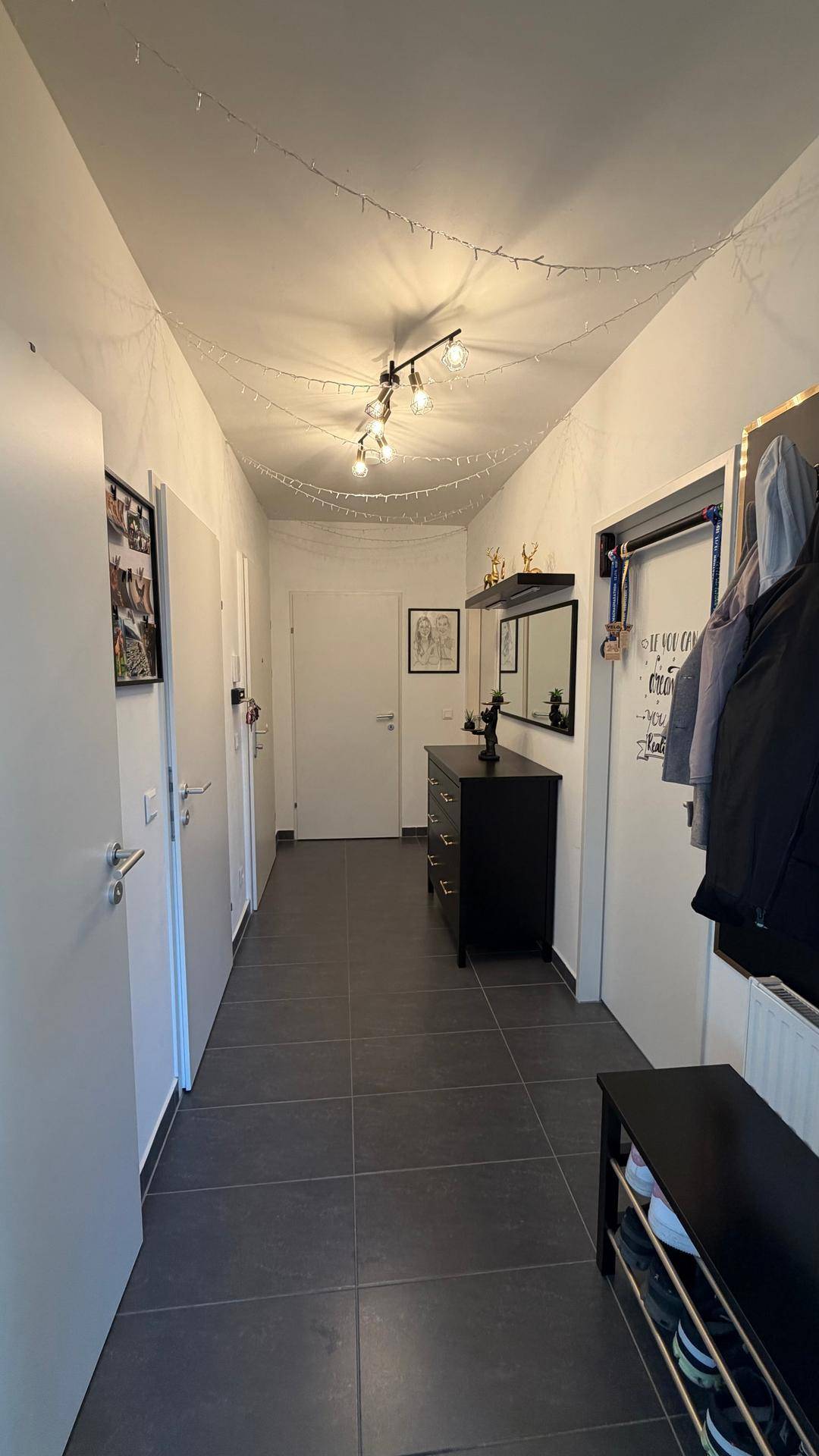 Heller Flur mit dunklem Fliesenboden, Spiegel und Garderobe, der zu weiteren Räumen führt.