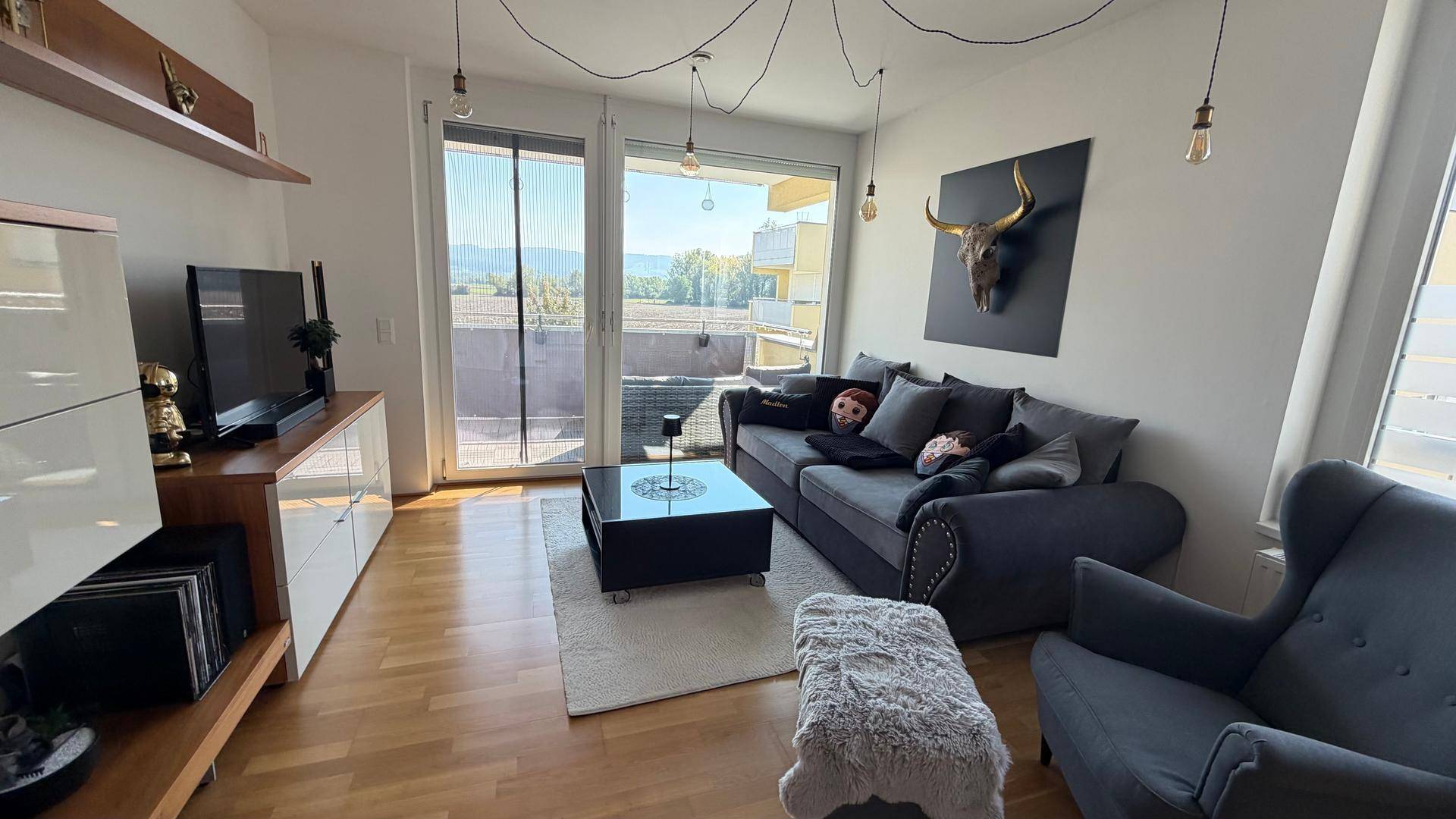 Gemütlicher Wohnbereich mit Sofa, TV-Möbel und hellem Holzboden, mit Balkonzugang.