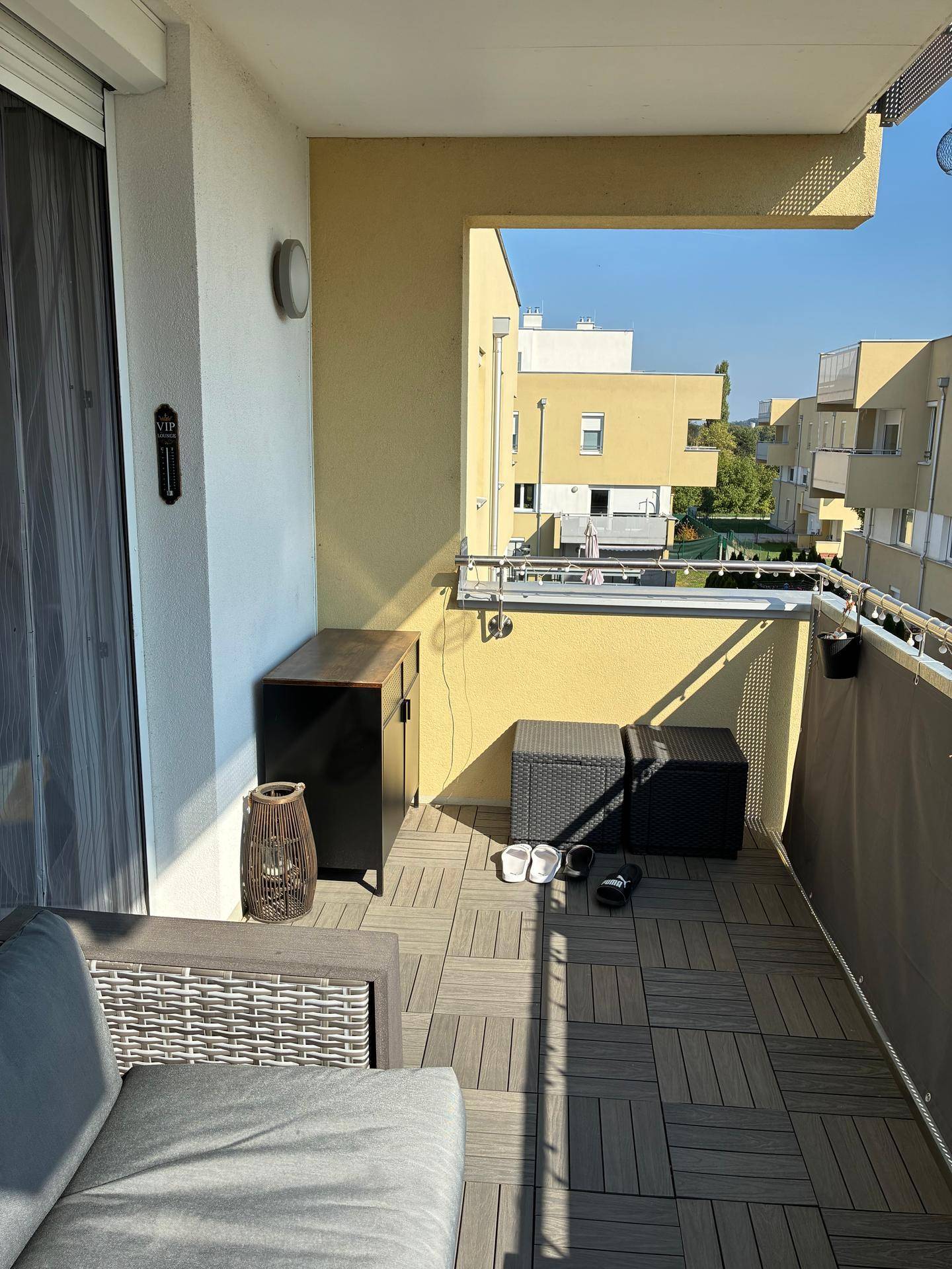 Gemütlicher Balkon mit Holzdielenboden und Outdoor-Sitzgelegenheiten, sonnig gelegen.
