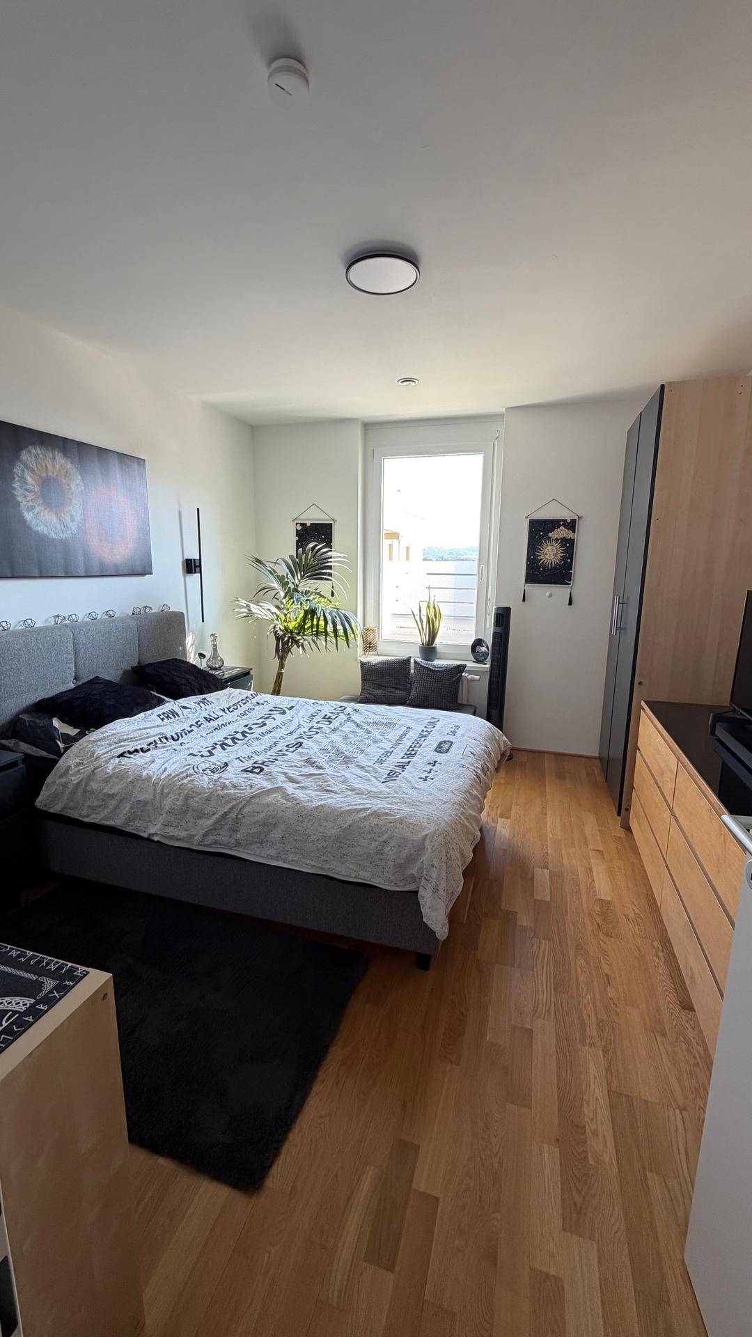 Geräumiges Schlafzimmer mit großem Bett, hellem Holzboden und Fenster für natürliches Licht.