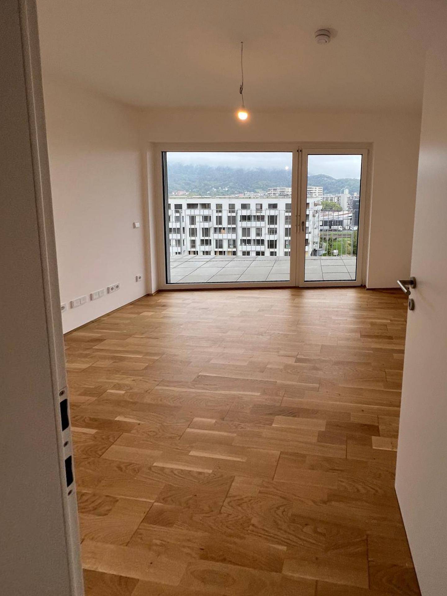 Geräumiges Zimmer mit Holzboden und großen Fenstern, die viel Tageslicht hereinlassen.