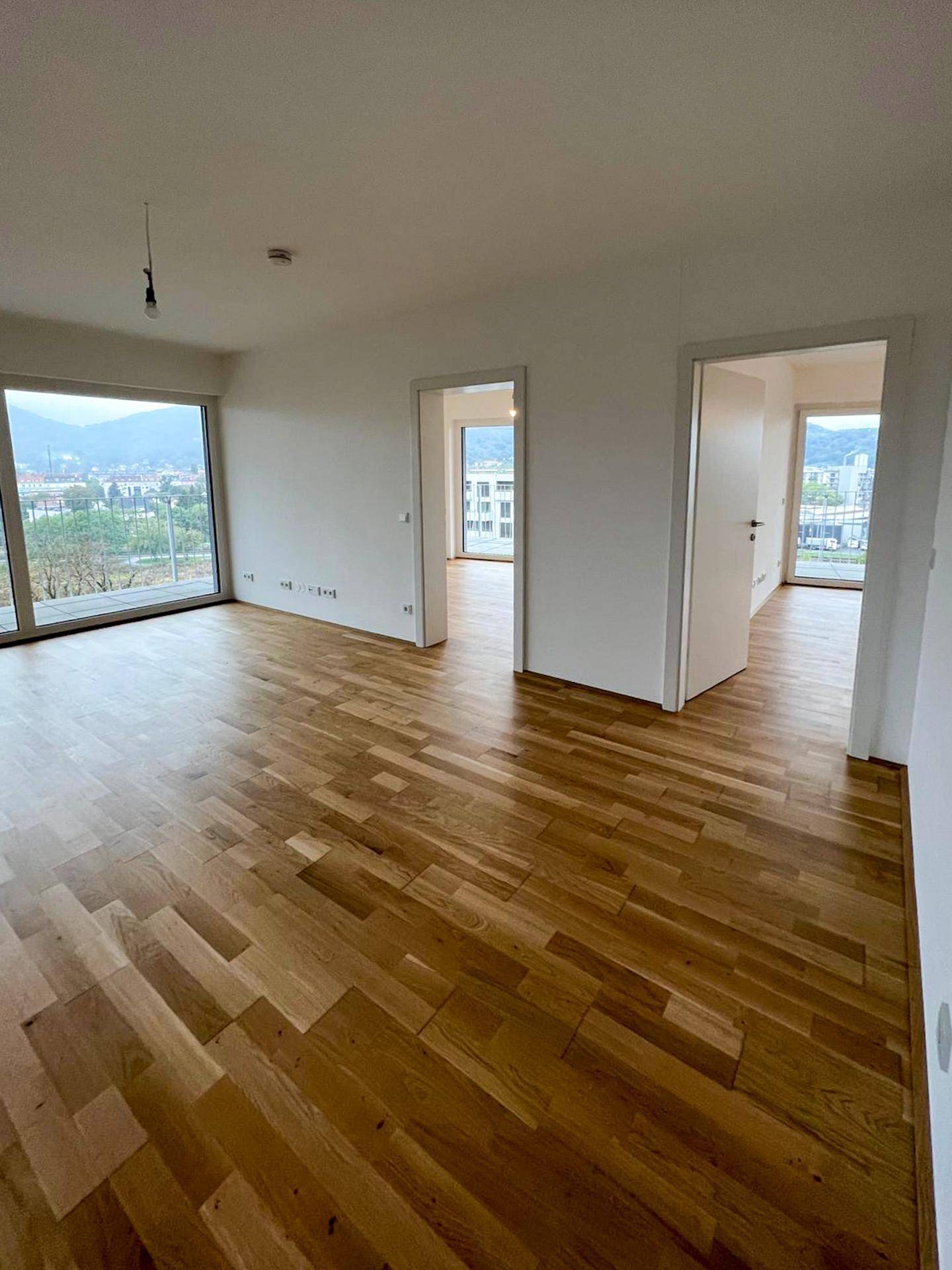 Heller Wohnbereich mit Holzboden und Zugang zu weiteren Zimmern sowie einem Balkon.