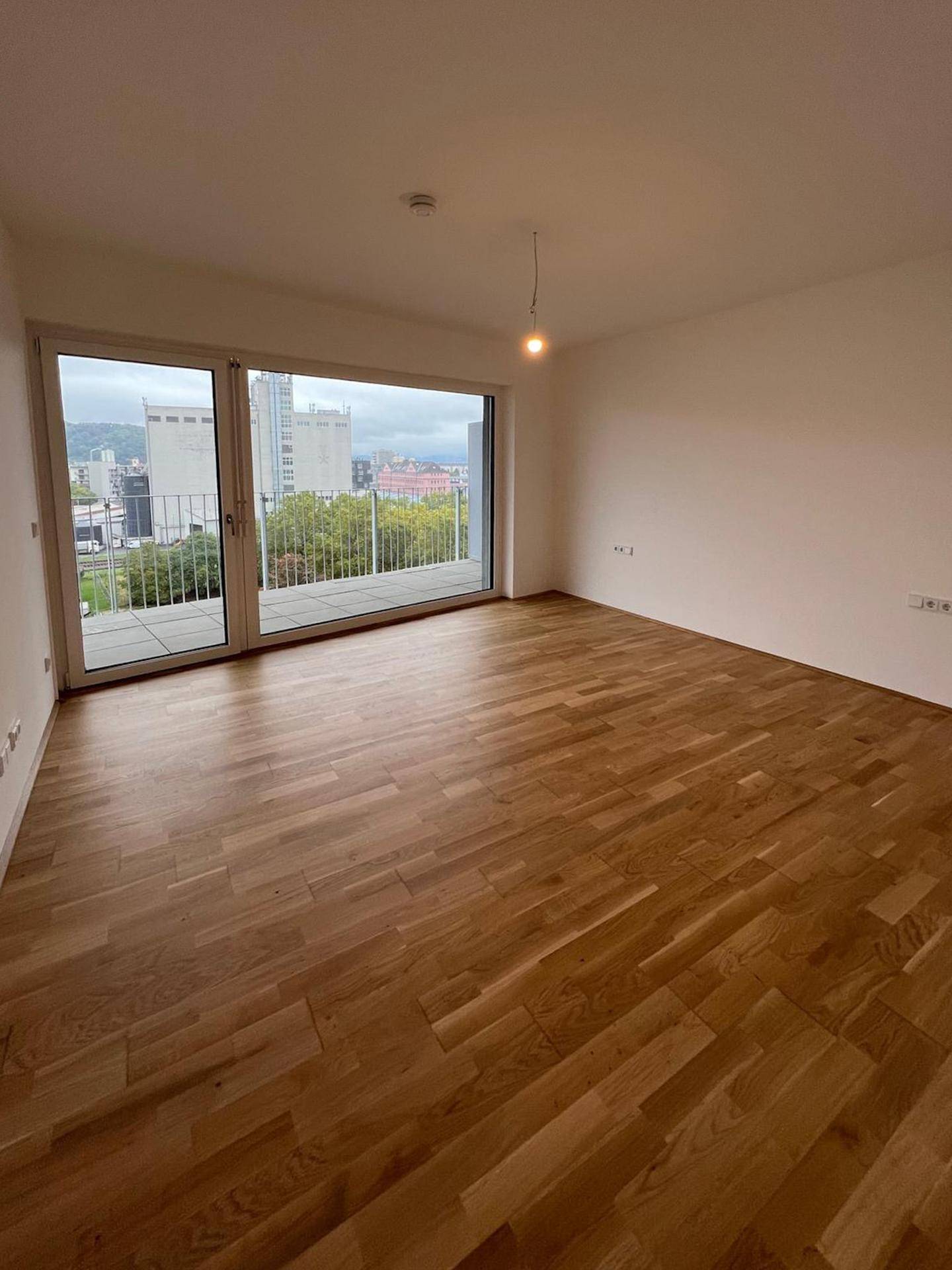 Helles Zimmer mit Holzboden und Zugang zu einem Balkon mit Stadtblick.