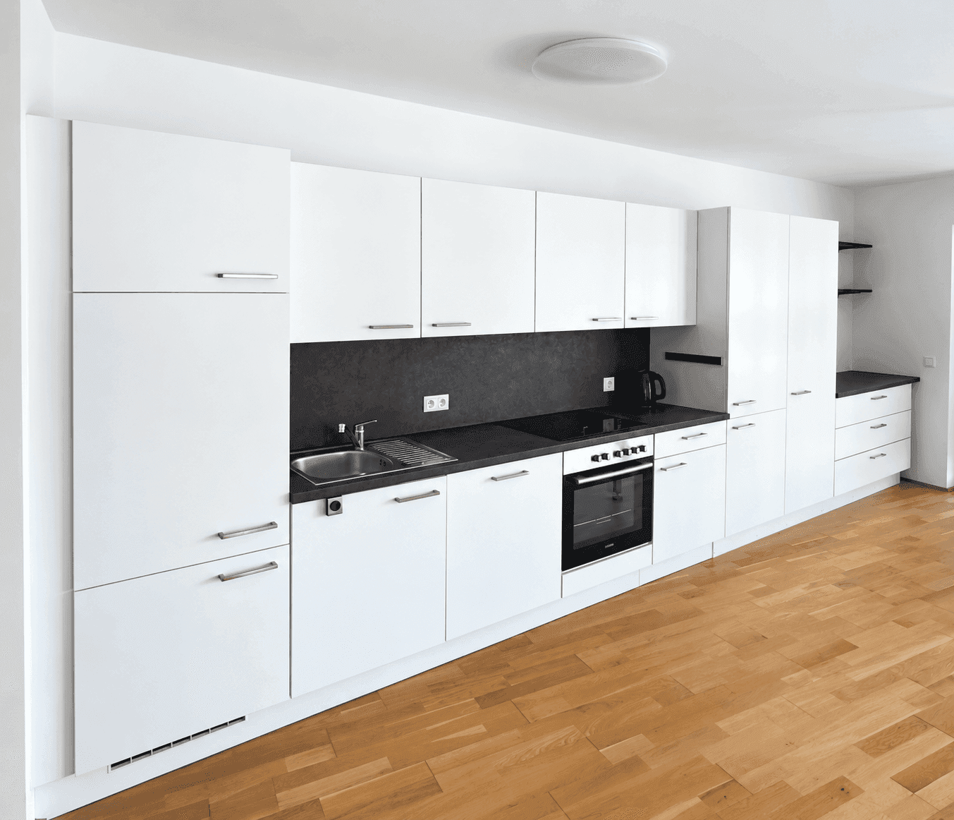Moderne Einbauküche mit weißen Fronten, dunkler Arbeitsplatte und integrierten Geräten.