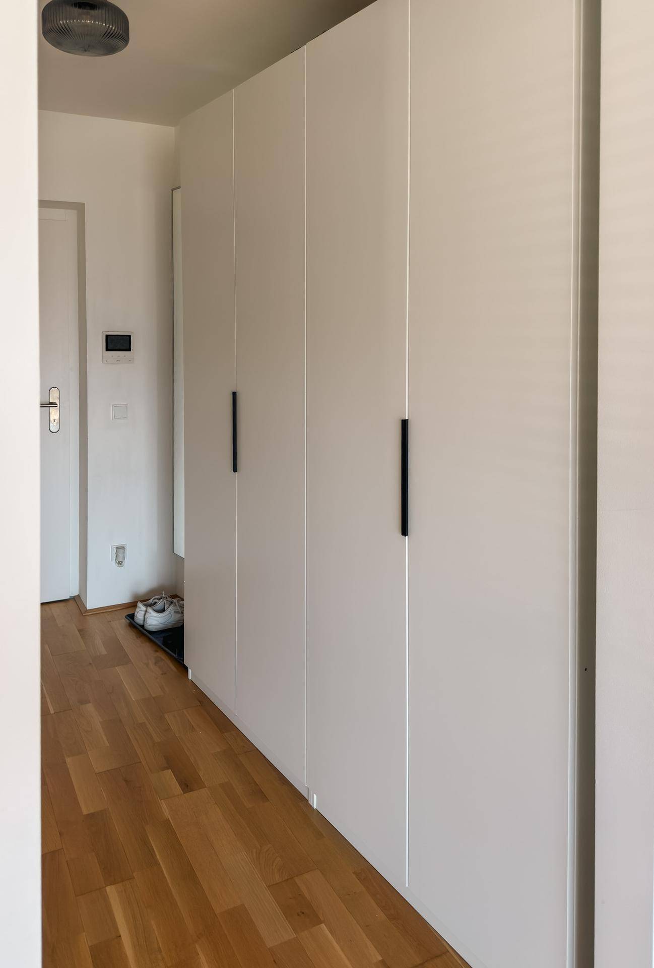 Heller Flur mit integrierten weißen Einbauschränken und Holzboden.