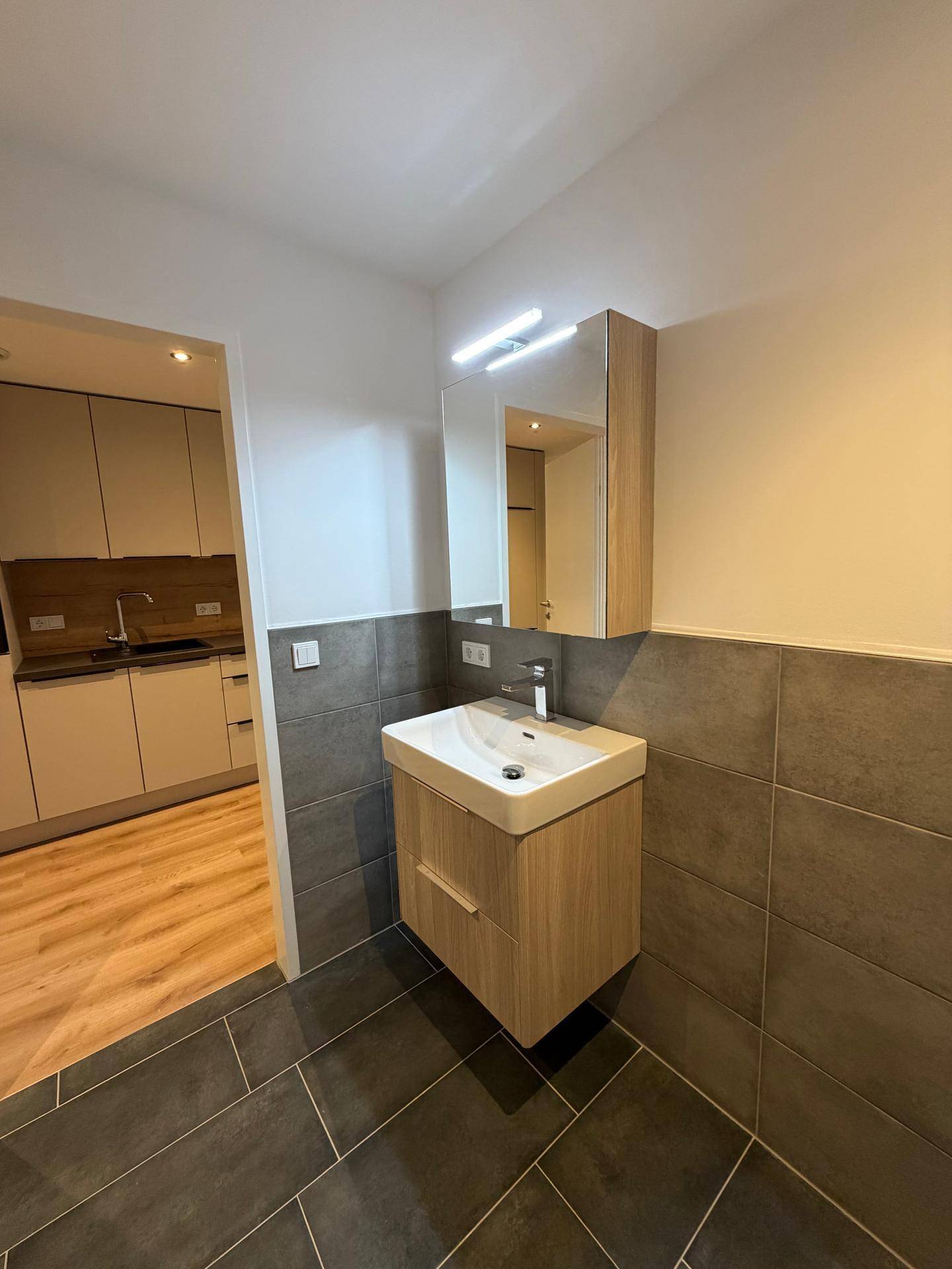 Modernes Badezimmer mit Einzelwaschbecken, Spiegelschrank und grauen Wand- und Bodenfliesen.