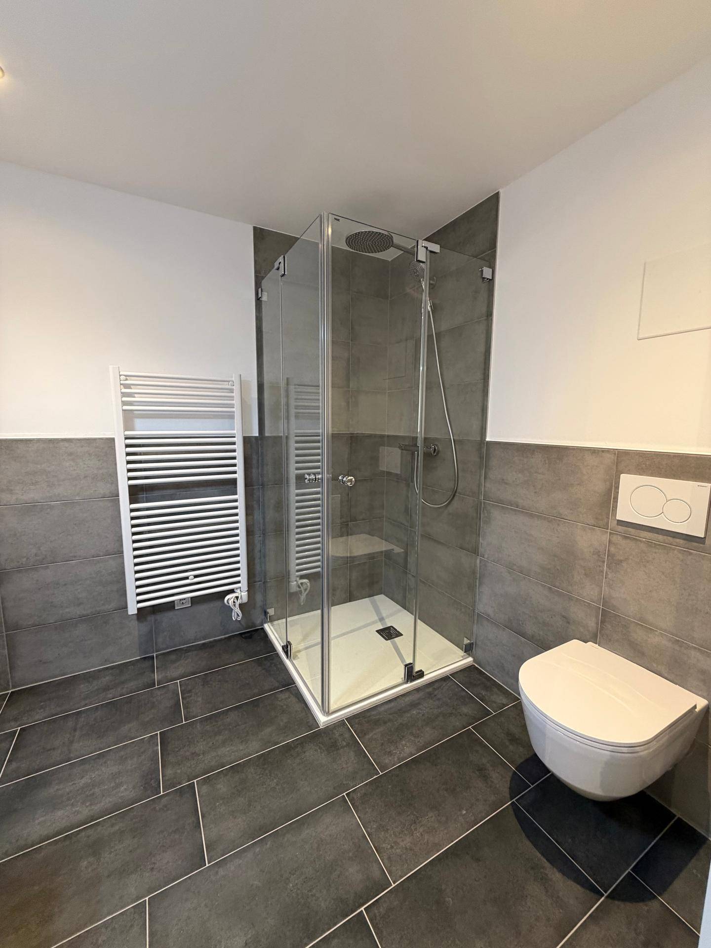 Helles Badezimmer mit großer Glasdusche, wandhängendem WC und praktischem Handtuchheizkörper.