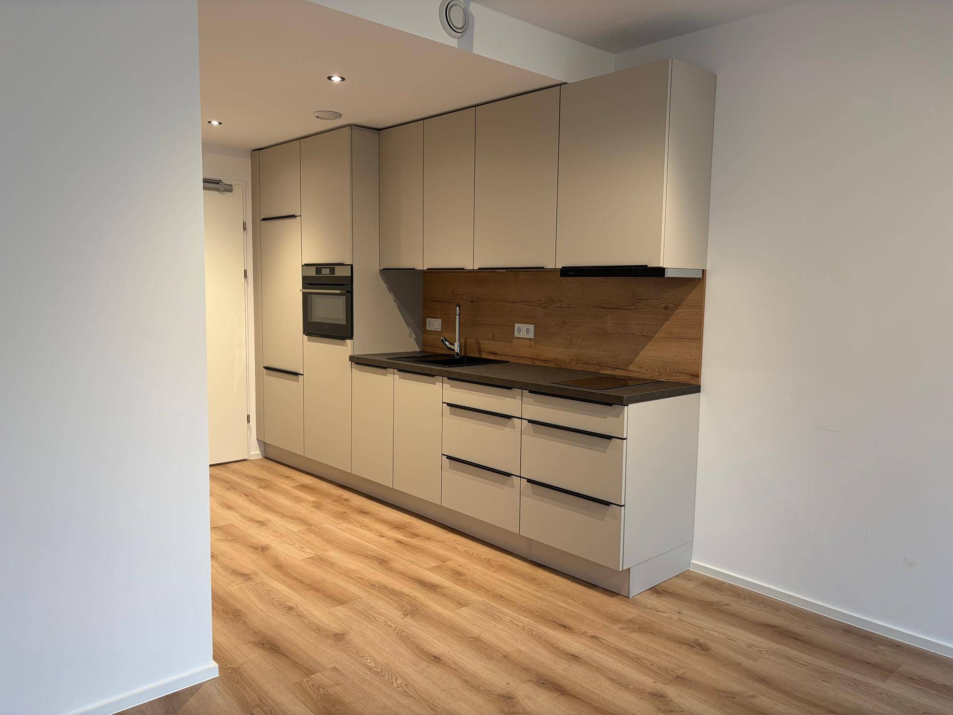 Moderne Einbauküche in hellem Beige mit integriertem Backofen und Holzrückwand.