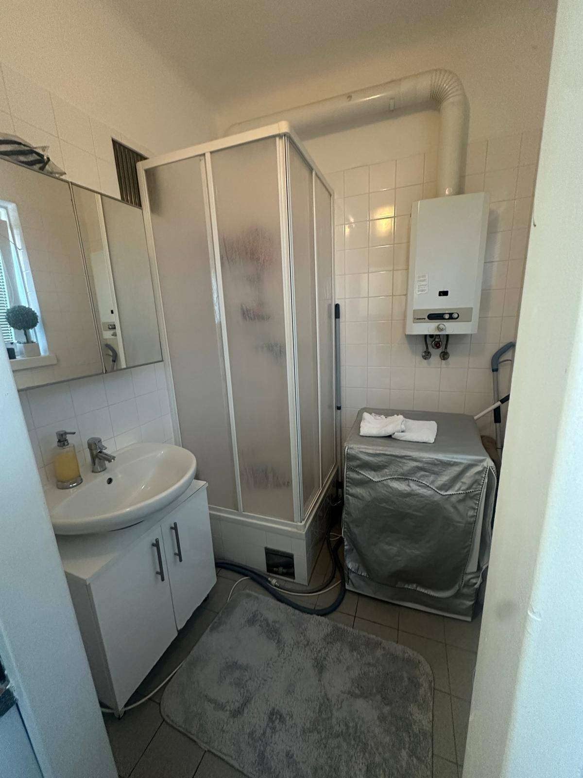 Badezimmer mit Duschkabine, Waschbecken und Waschmaschine, gefliest.