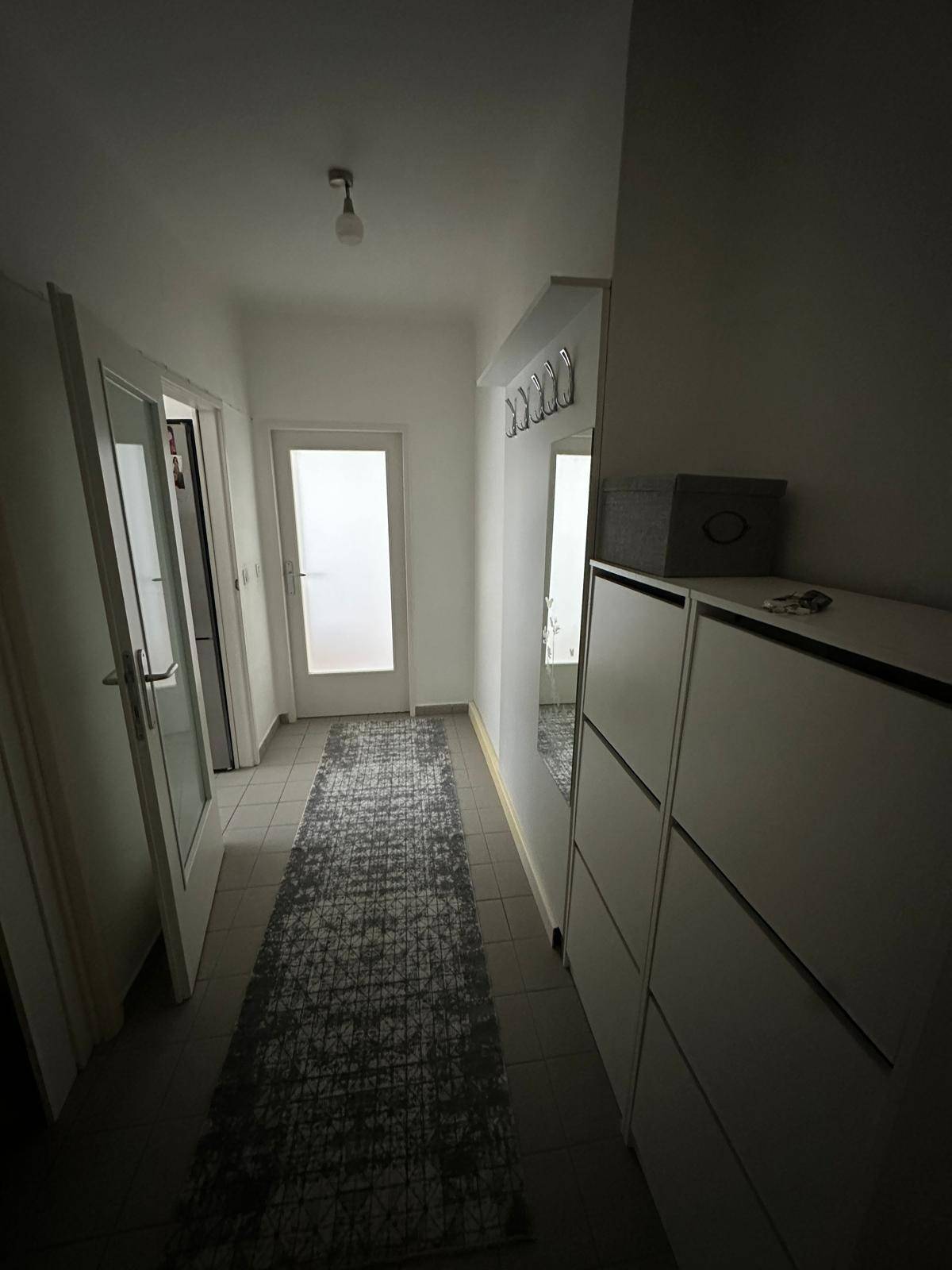 Heller Flur mit Schuhschrank, Spiegel und Garderobe, gefliestem Boden.