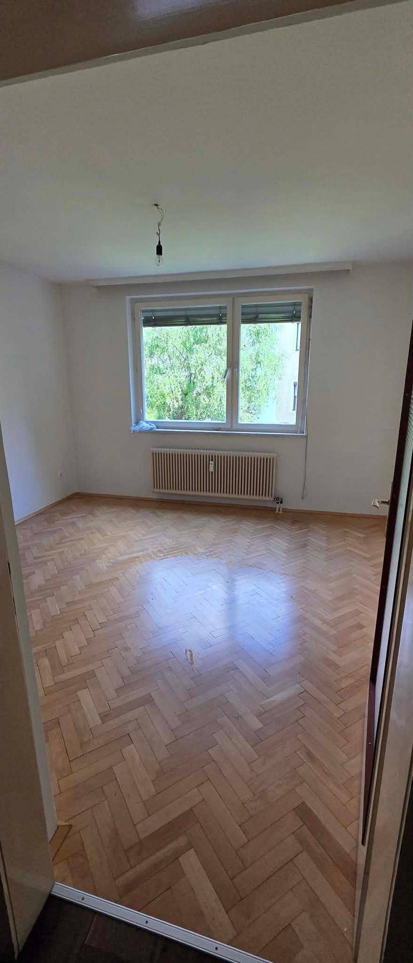 Helles Zimmer mit klassischem Fischgrätparkett, großem Fenster und Heizkörper.