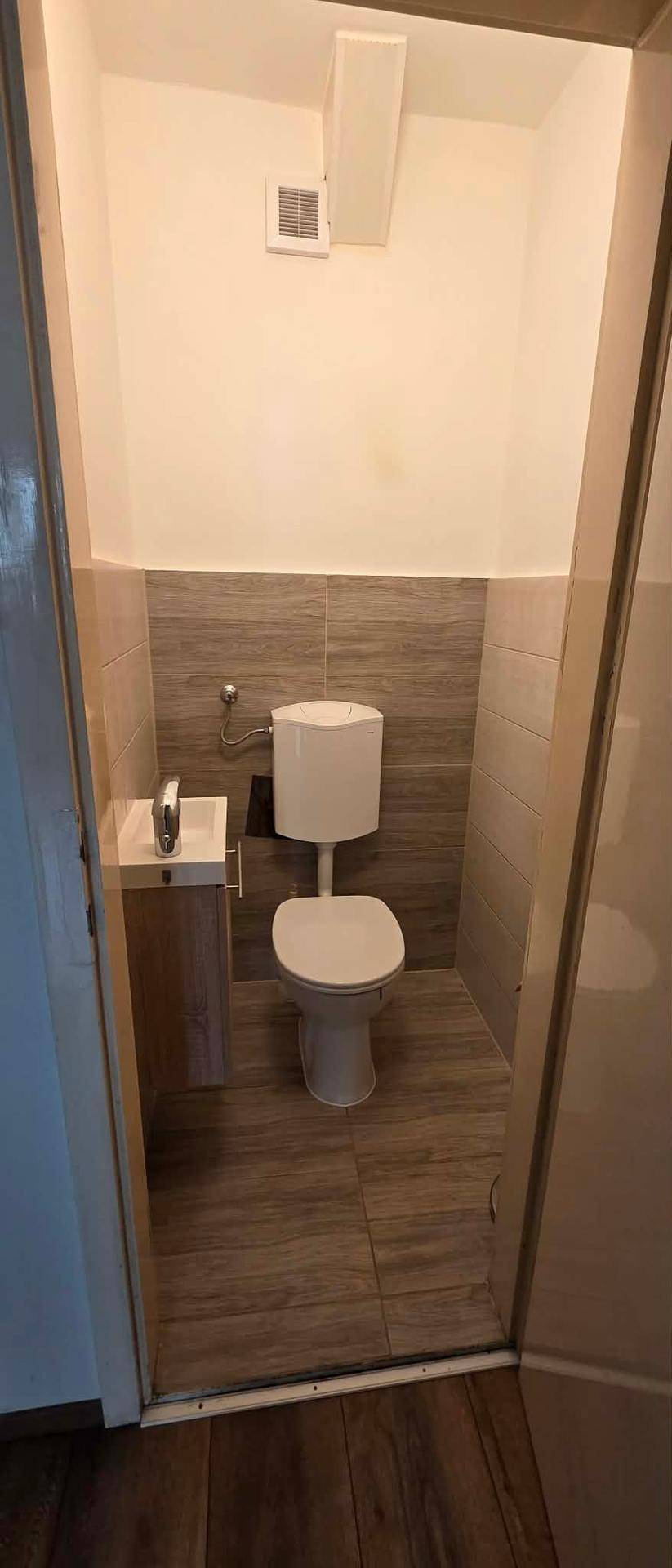 Kleines Gäste-WC mit Toilette, Handwaschbecken und modernen Fliesen an den Wänden.