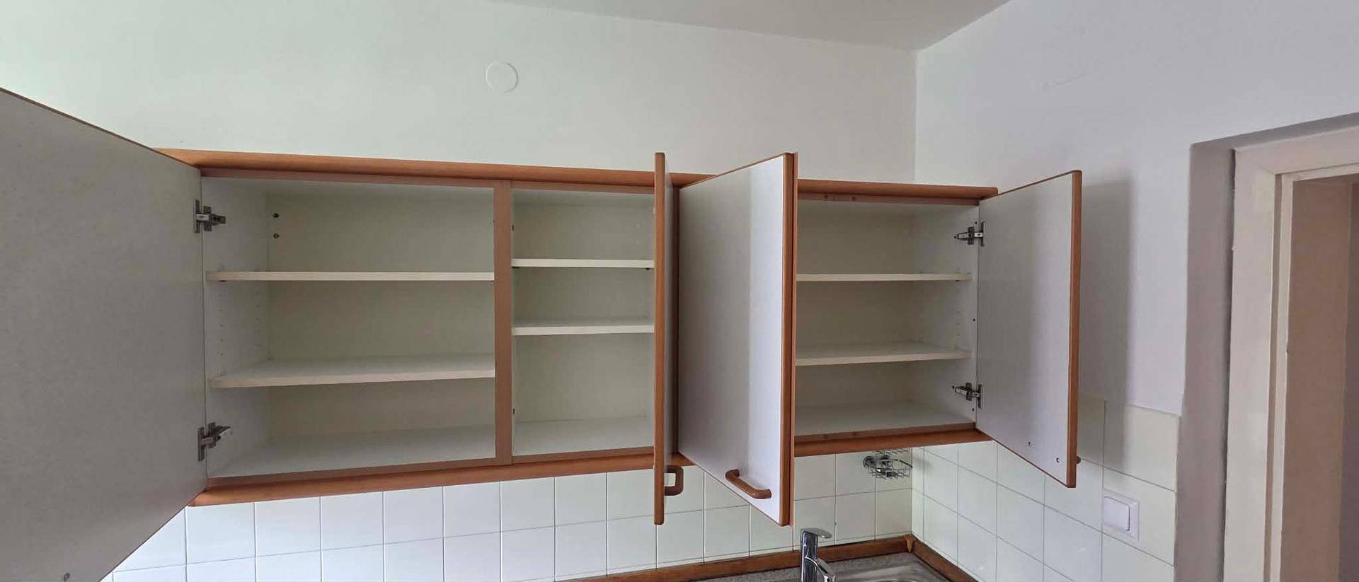 Offene Küchenoberschränke mit Regalböden und gefliestem Spritzschutz in einer hellen Küche.