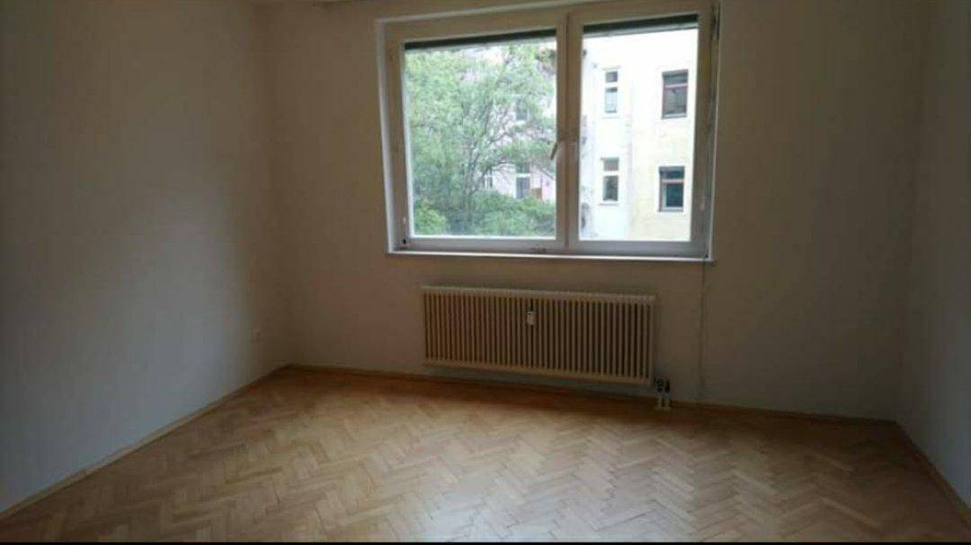 Leeres Zimmer mit klassischem Fischgrätparkett, großem Fenster und Heizkörper unter dem Fenster.