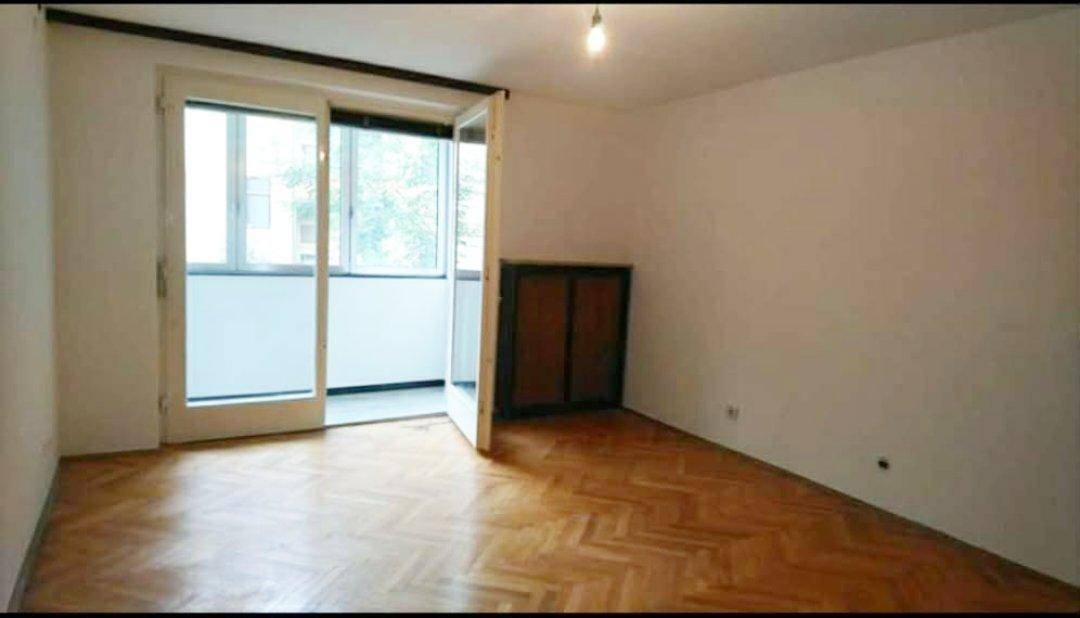 Heller Raum mit Fischgrätparkett und direktem Zugang zu einem Balkon durch eine breite Tür.