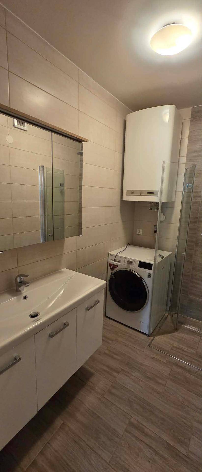 Funktionales Badezimmer mit Waschbecken, Spiegelschrank, Dusche und integrierter Waschmaschine.