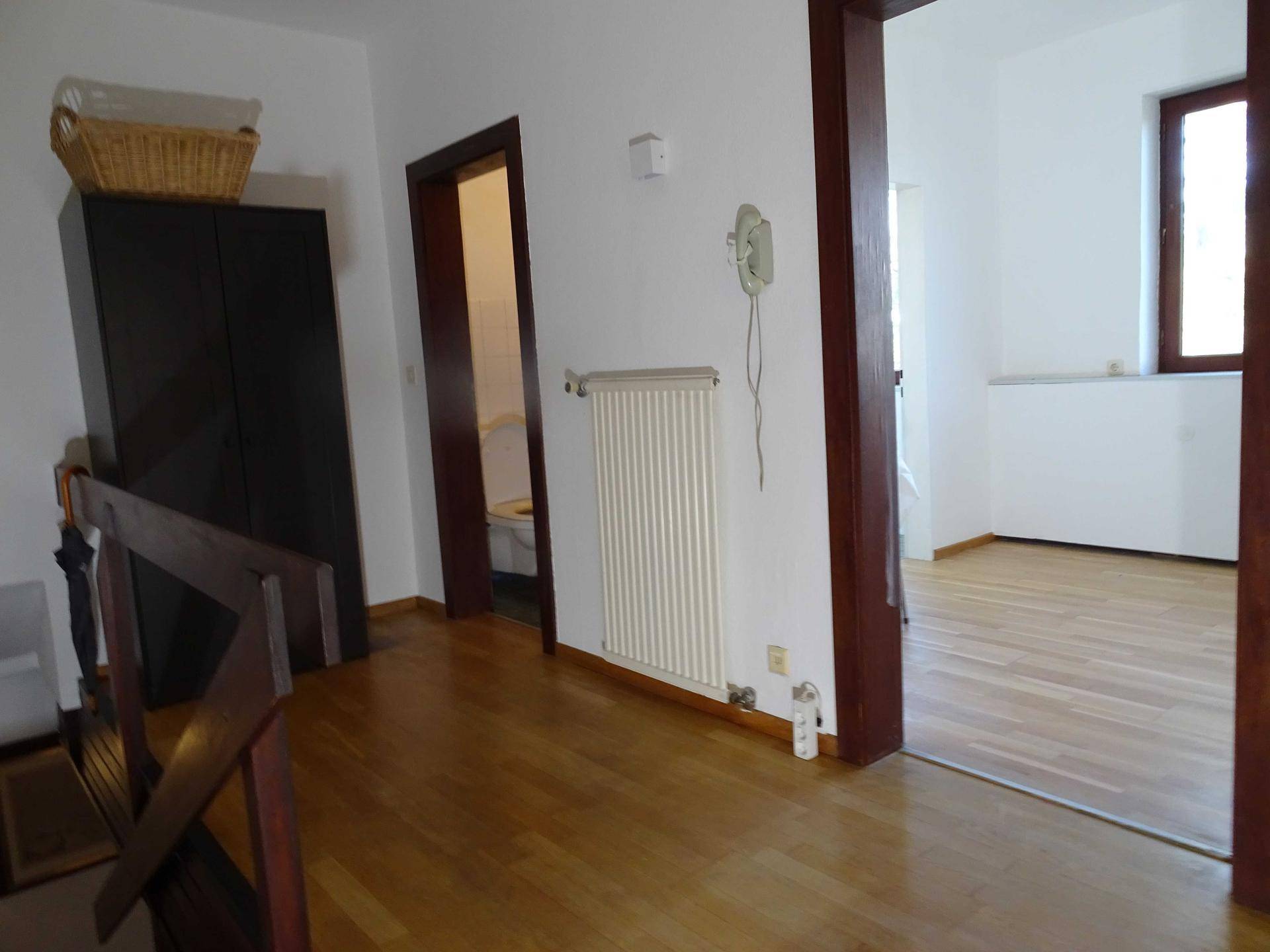 Flur mit Holzboden, dunklem Schrank und Blick in ein kleines Gäste-WC.