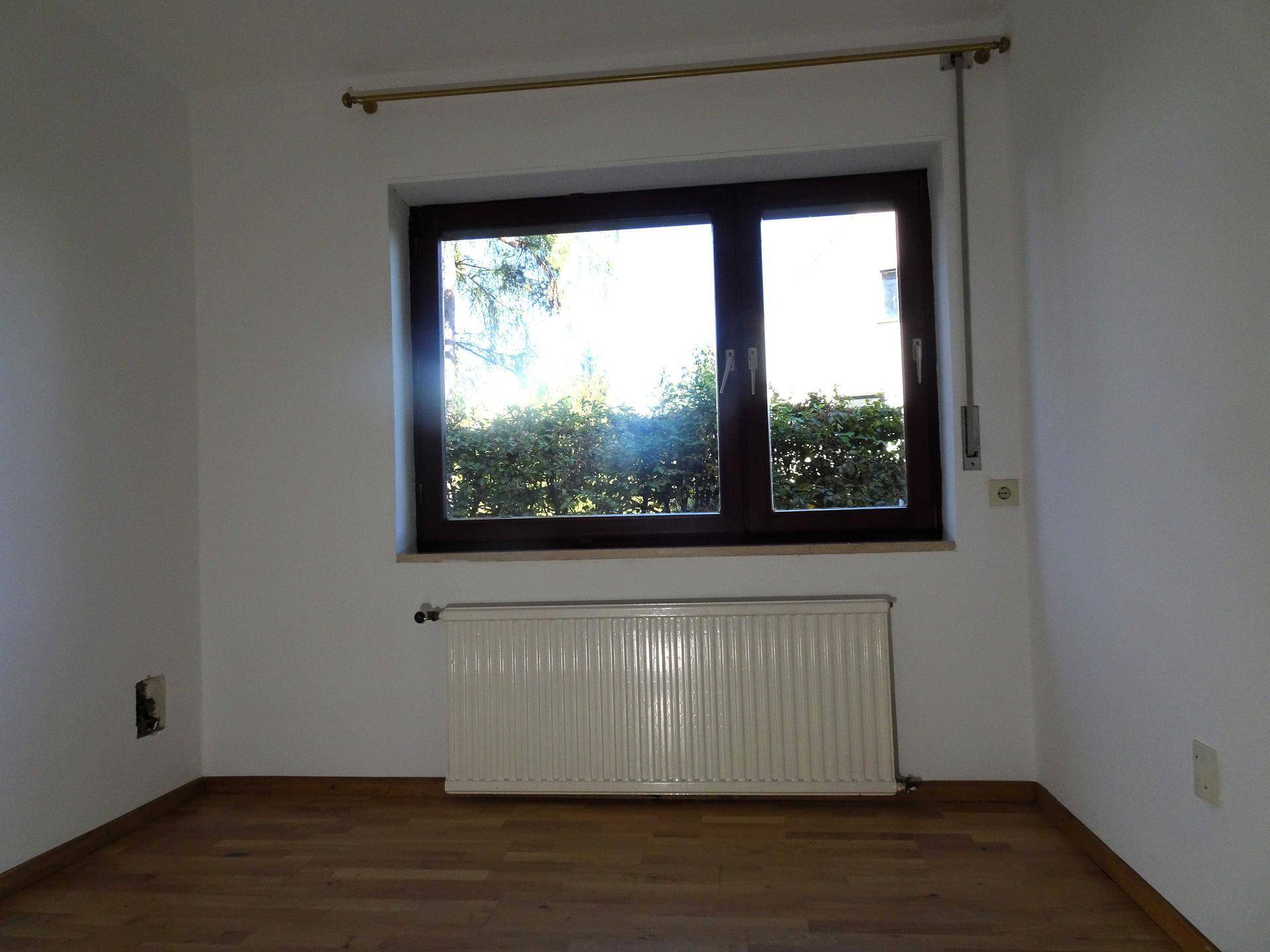 Kleineres Zimmer mit Holzboden, Heizkörper und Fenster mit Blick auf die Umgebung.