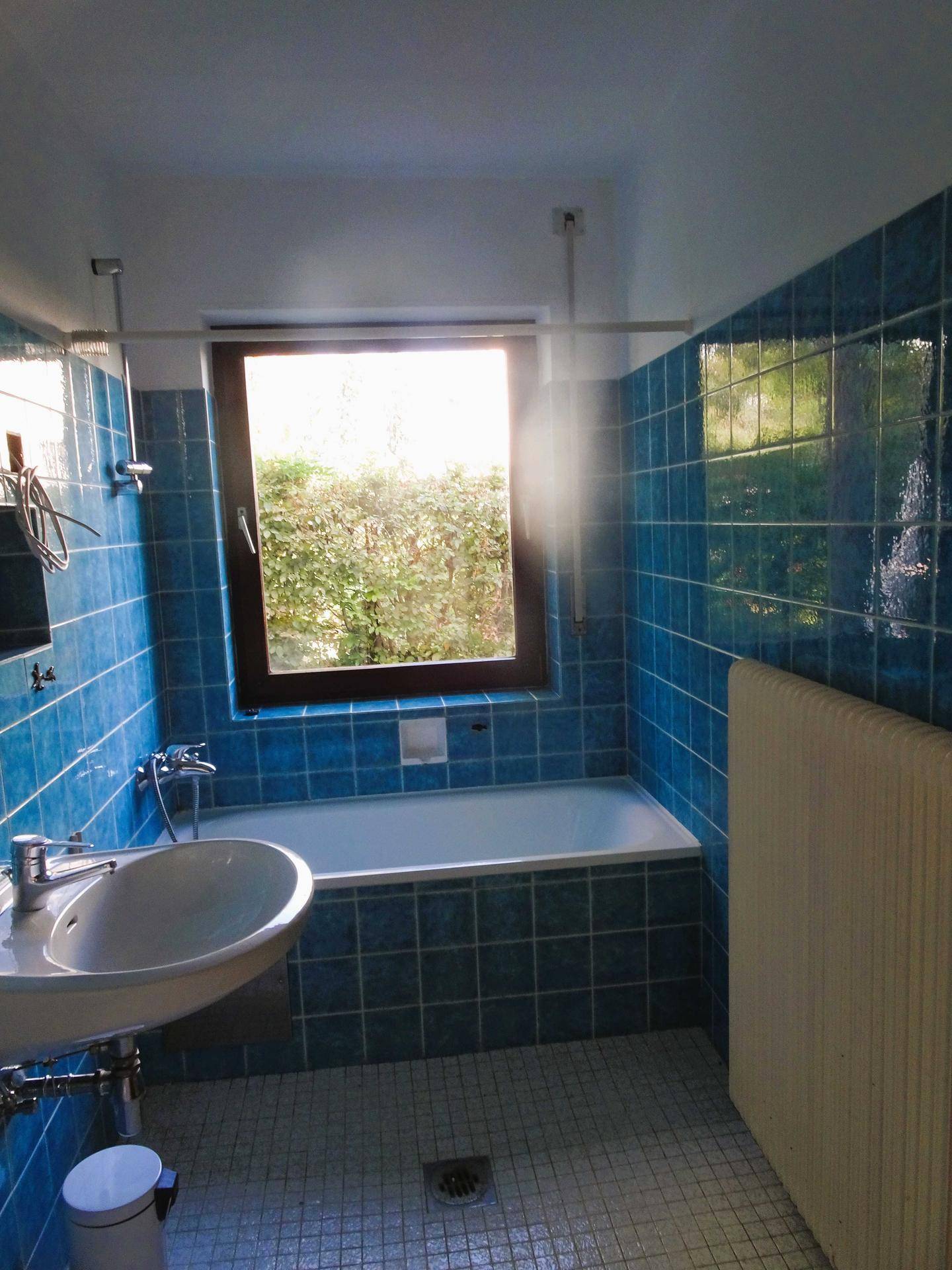 Badezimmer mit blauen Fliesen, Badewanne, Waschbecken und Fenster für Tageslicht.