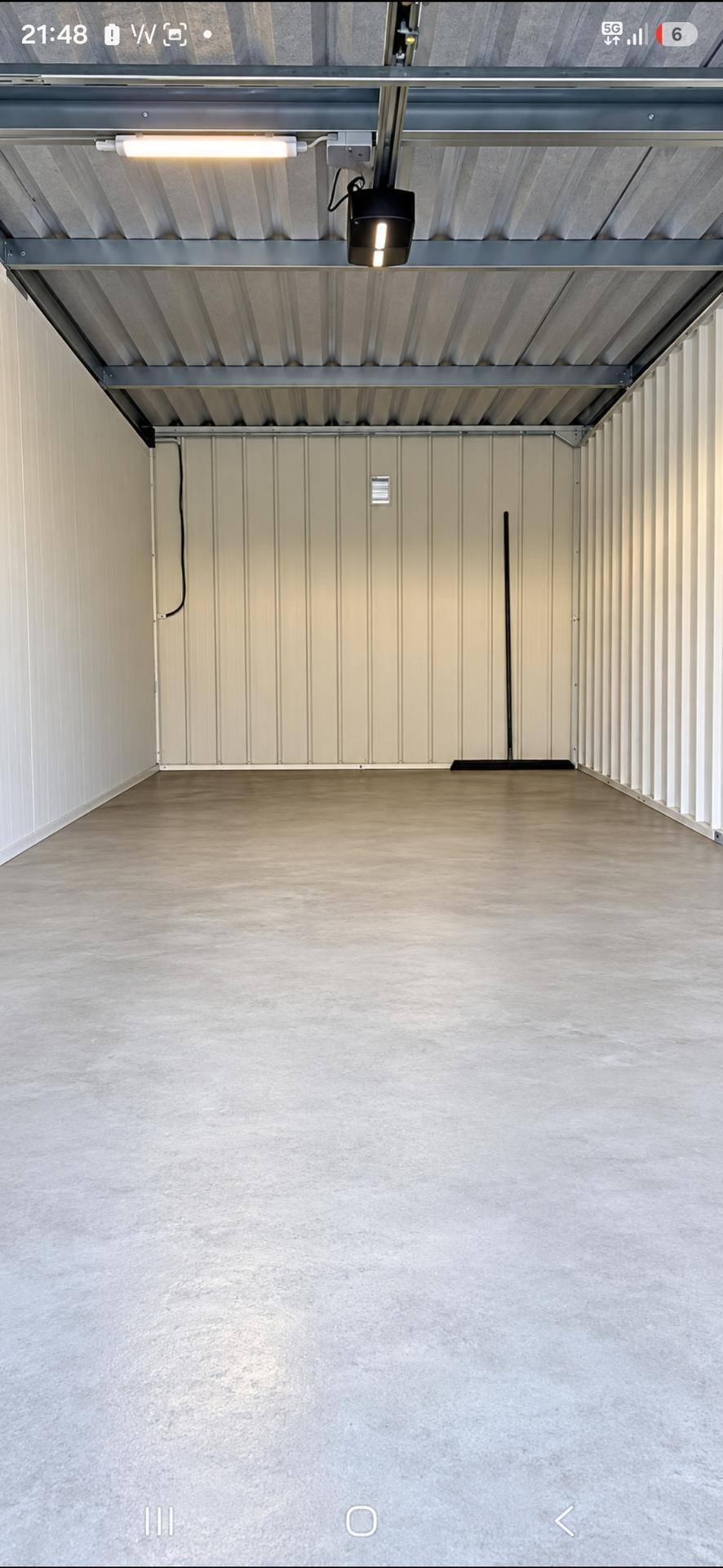Leere und saubere Garagenbox mit Betonboden, Wellblechwänden und Deckenbeleuchtung, bereit zur Nutzung.
