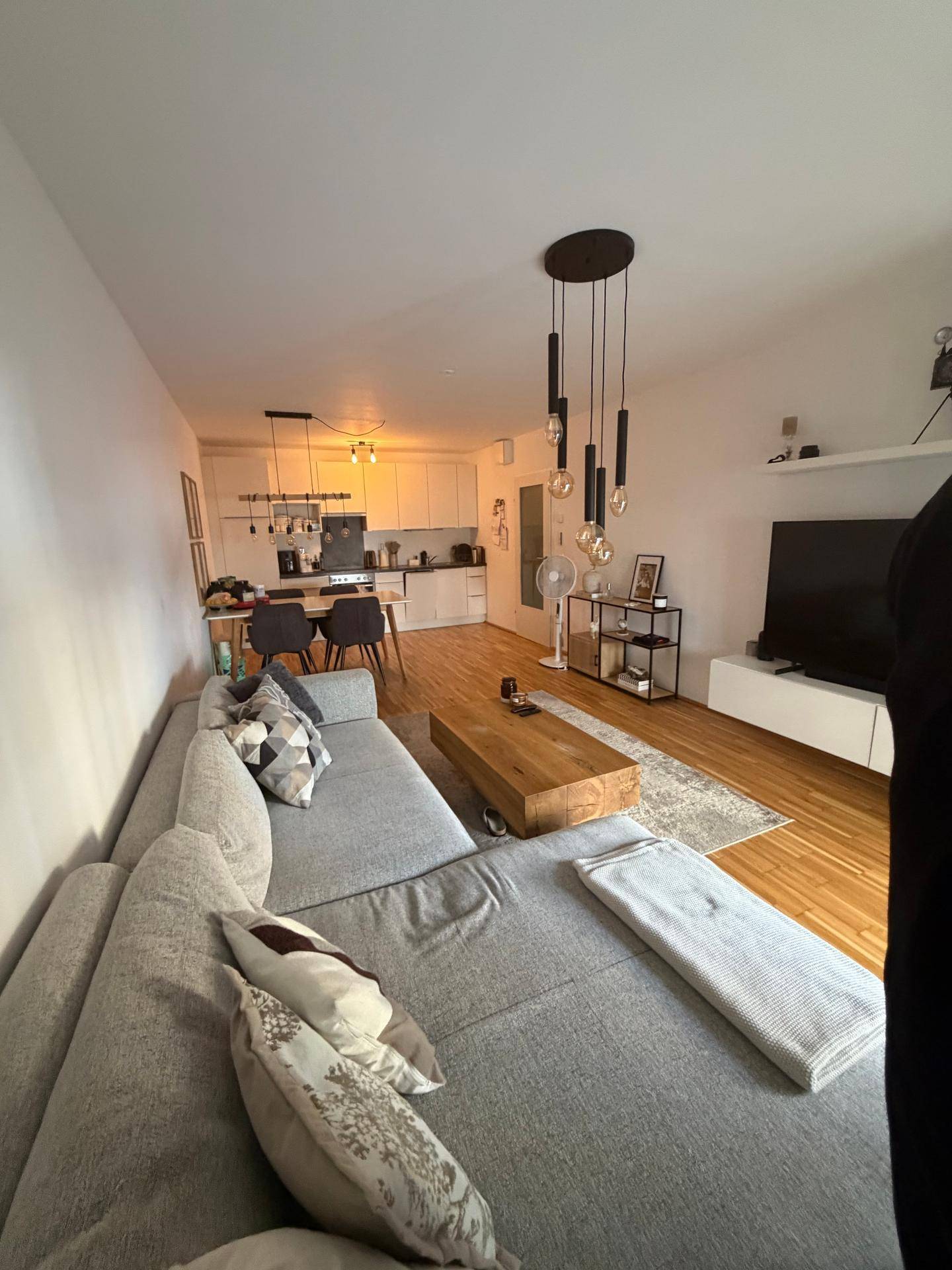 Offener Wohnbereich mit integrierter Küche, großem Ecksofa und modernem Holz-Couchtisch.