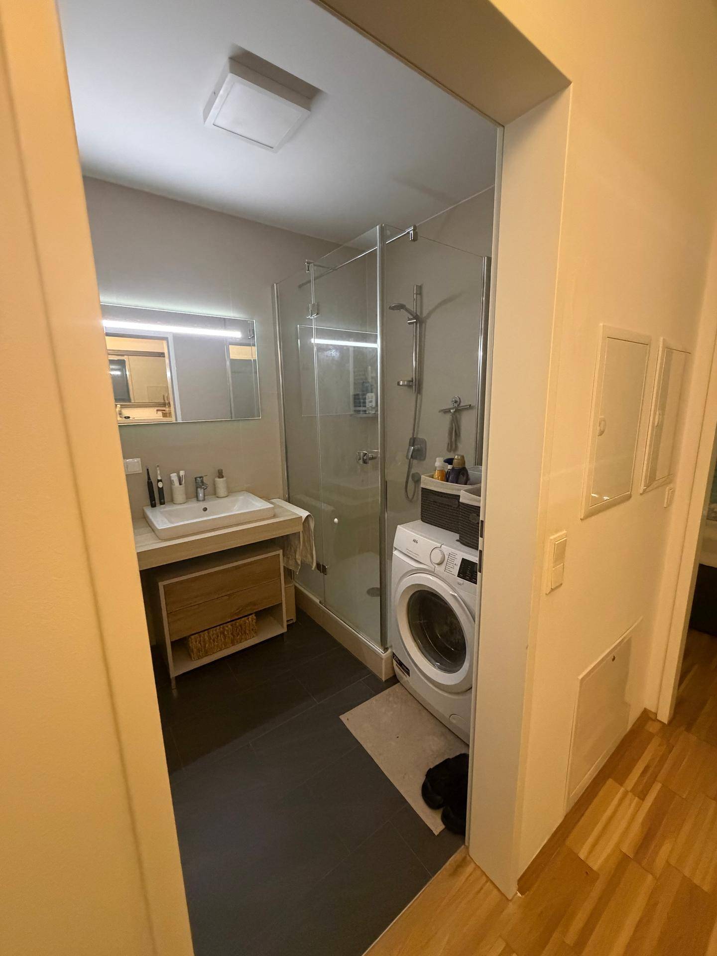 Modernes Badezimmer mit begehbarer Dusche, Waschbecken und integrierter Waschmaschine.