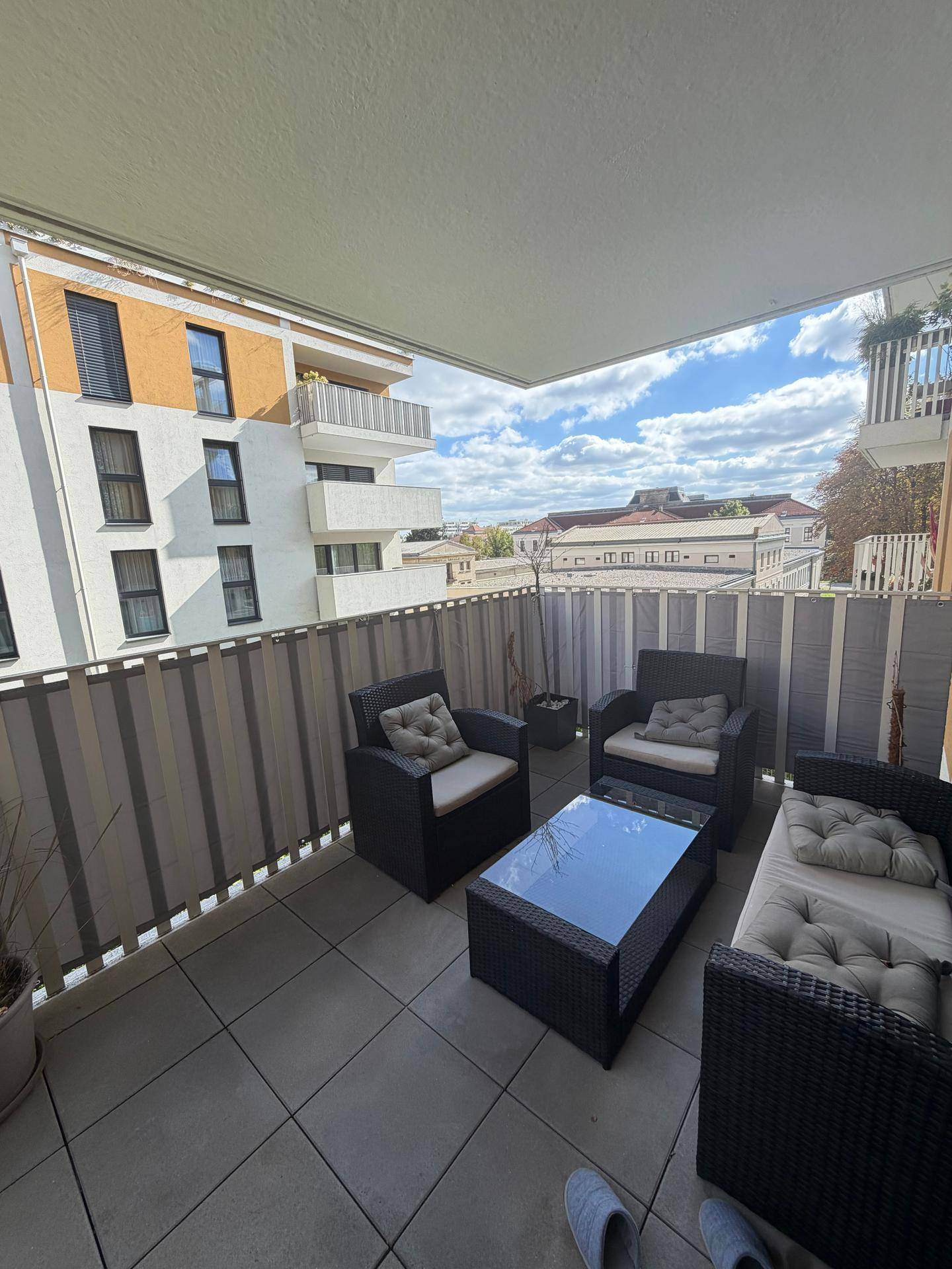 Möblierter Balkon mit Rattan-Sitzgruppe und Blick auf die umliegenden Gebäude.