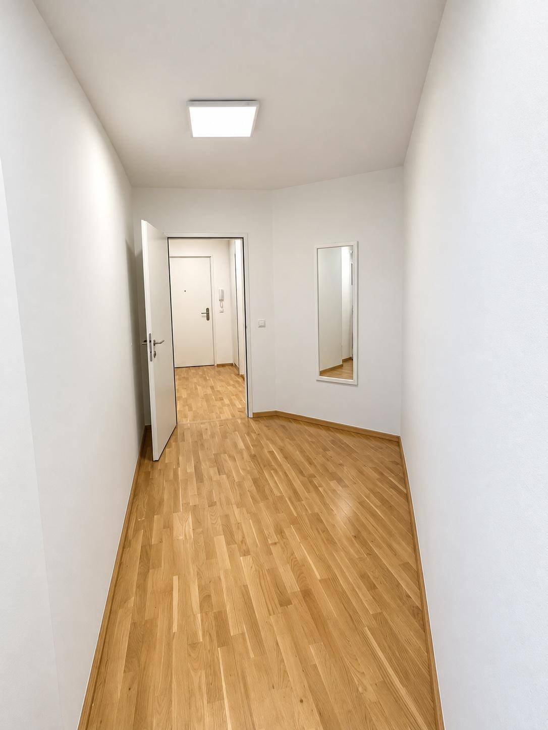 Heller Flur mit Holzboden und einem Spiegel, der zu weiteren Räumen führt.