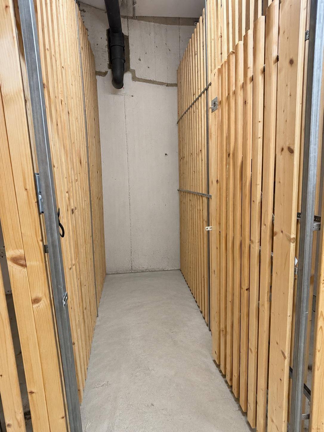 Praktischer Abstellraum mit Holzlattenwänden und Betonboden, ideal für zusätzlichen Stauraum.