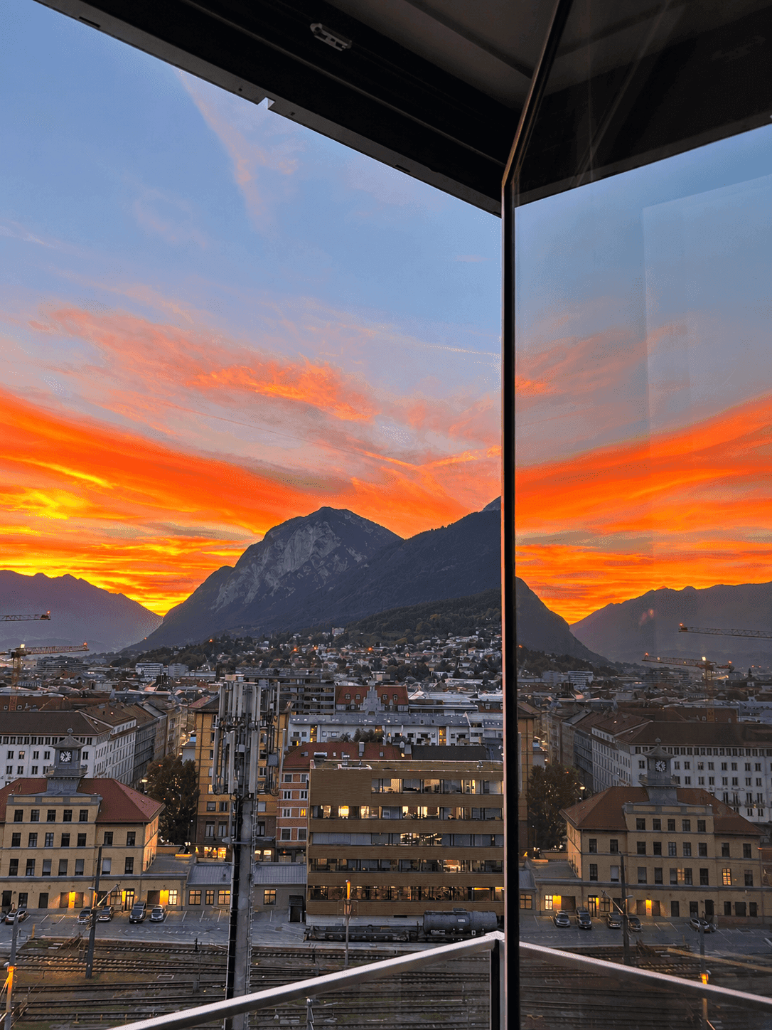 Spektakulärer Sonnenuntergang über der Stadt und den Bergen, gesehen durch ein großes Fenster.