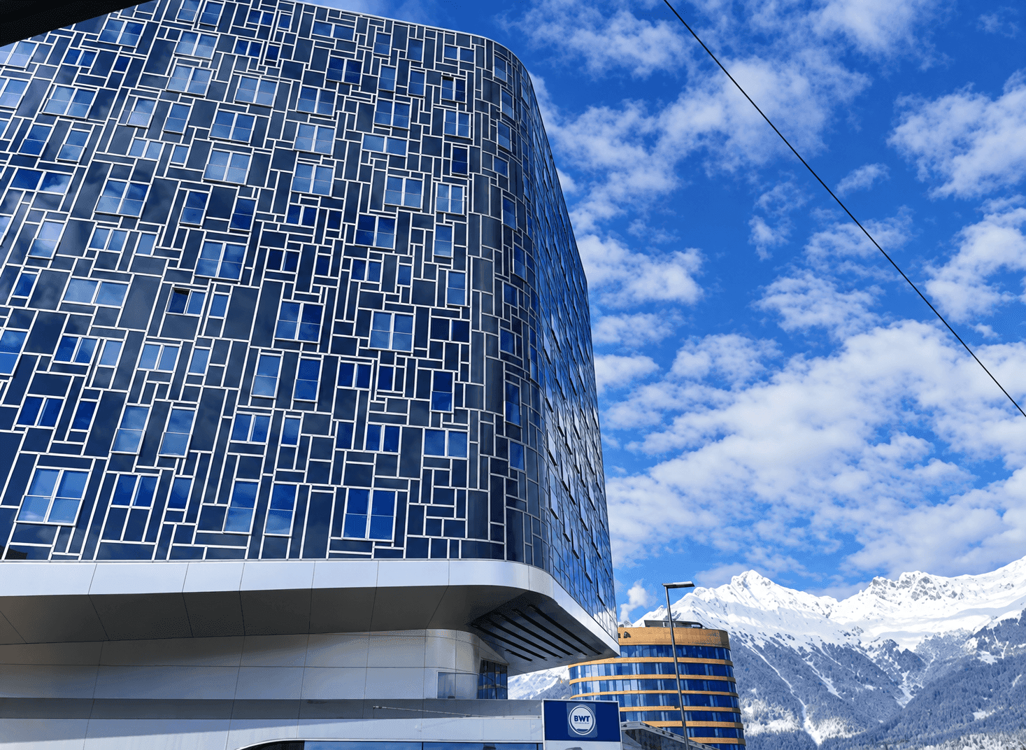 Auffälliges modernes Gebäude mit blauer Fassade und geometrischen Fenstern vor Bergkulisse.