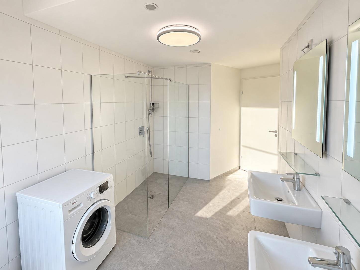 Geräumiges Badezimmer mit Doppelwaschbecken, großer begehbarer Dusche und Waschmaschine.