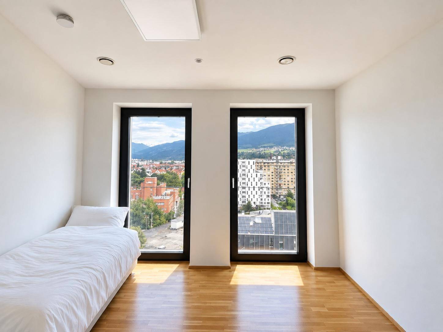Kleines Schlafzimmer mit Einzelbett, Holzboden und zwei Fenstern mit Stadt- und Bergblick.