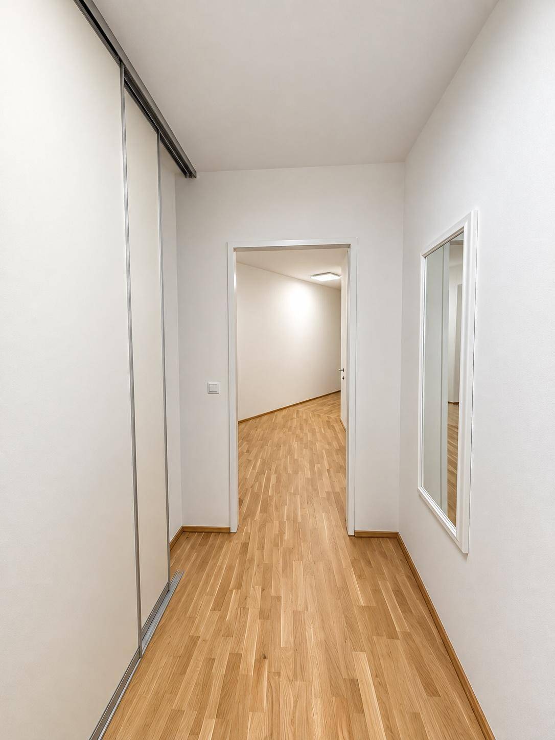 Langer Flur mit Holzboden, Einbauschränken und einem Spiegel, der den Raum erweitert.