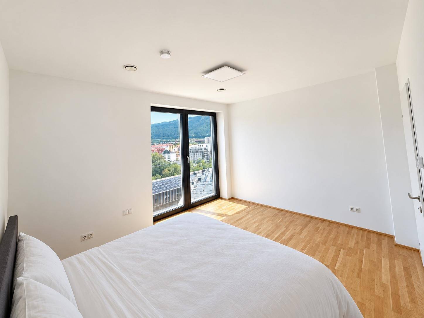 Helles Schlafzimmer mit Holzboden und Fenster, das einen Blick auf die Stadt und die Berge bietet.