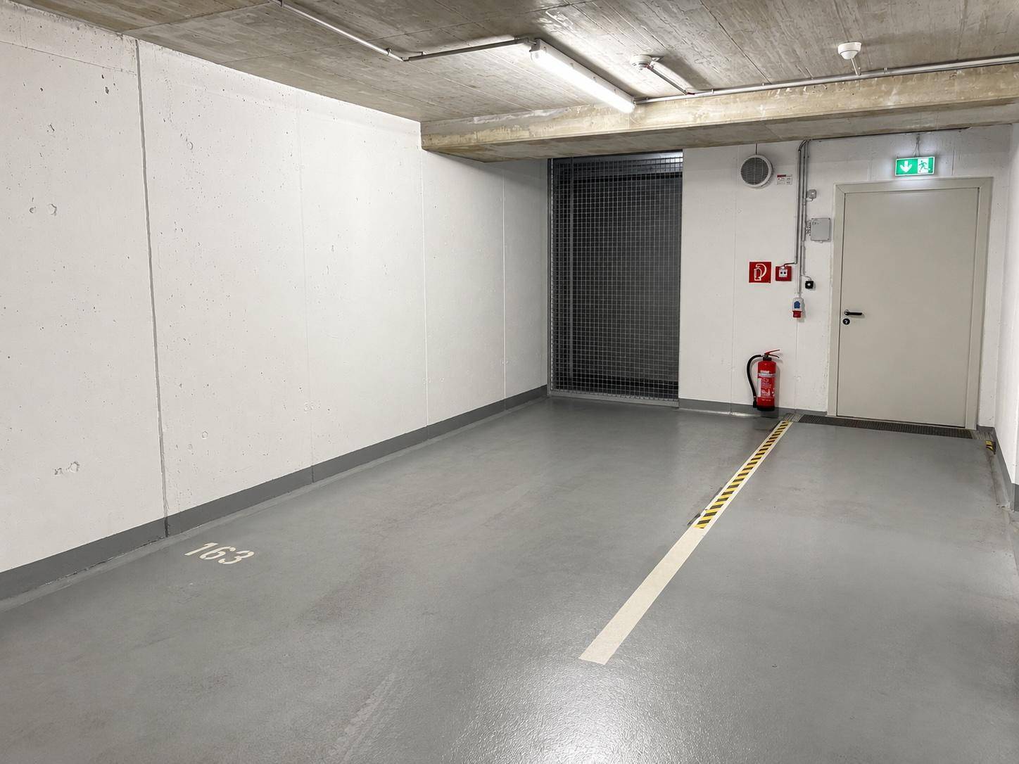 Geräumiger Tiefgaragenstellplatz mit Betonboden und Sicherheitsausstattung.