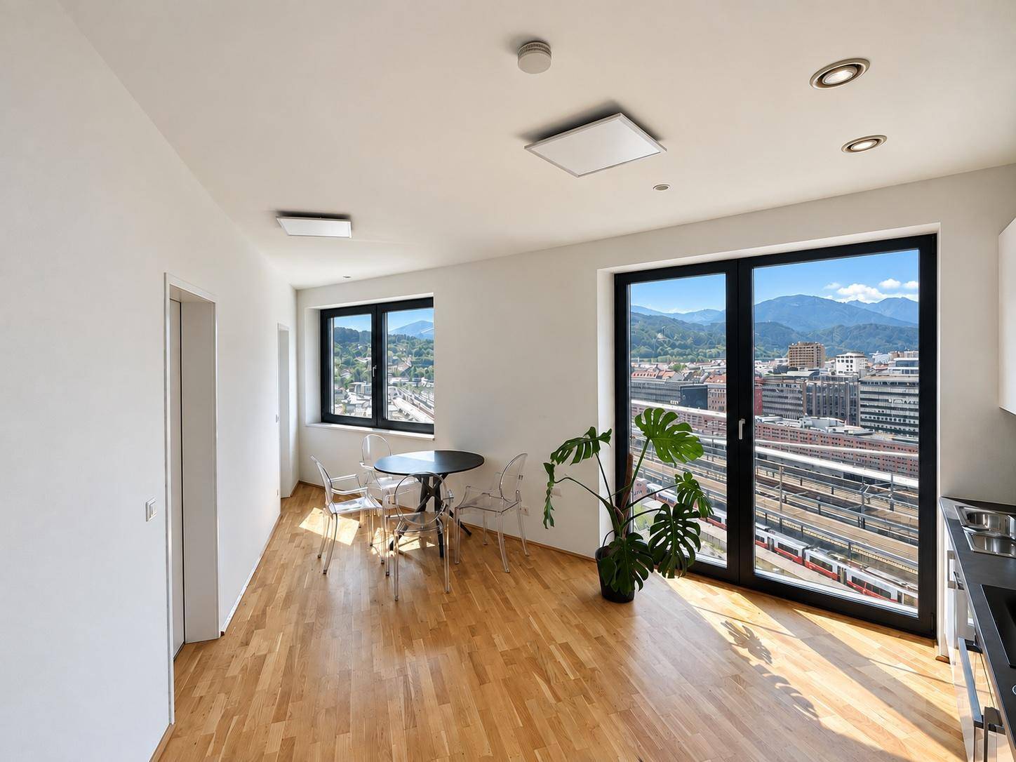 Heller Wohn-Essbereich mit Holzboden, Esstisch und Blick auf die Stadt und Bahngleise.
