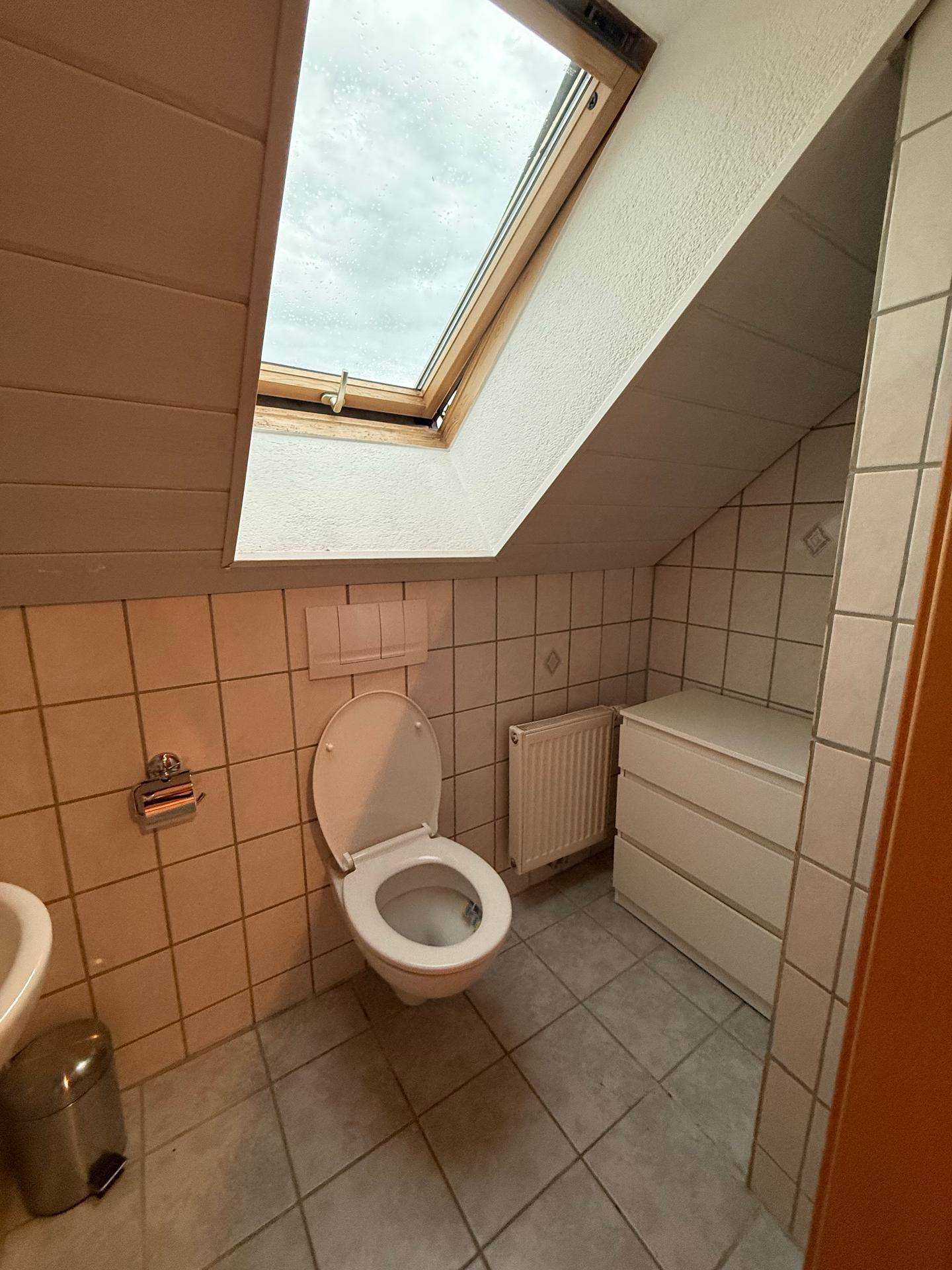 Kleines WC mit Fliesen, Dachfenster und Heizkörper, praktisch unter der Dachschräge gelegen.