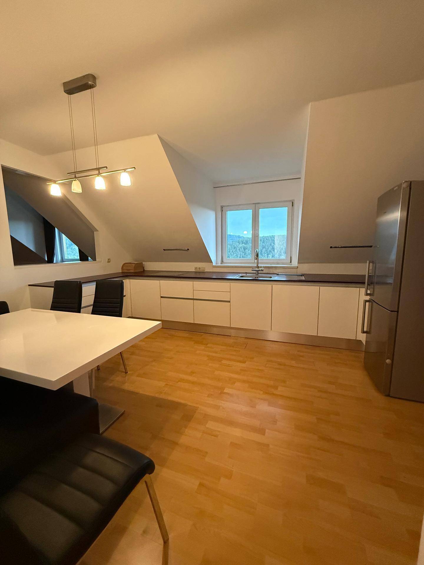 Funktionale Küche im Dachgeschoss mit weißen Schränken, Essbereich und großem Kühlschrank.