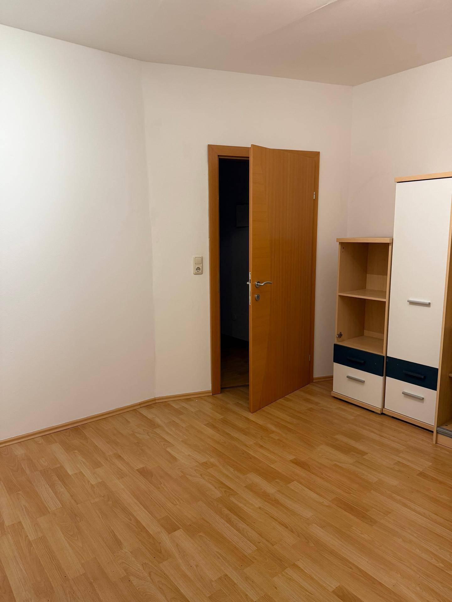 Helles Schlafzimmer mit Laminatboden und einfacher Möblierung, bereit zur individuellen Gestaltung.