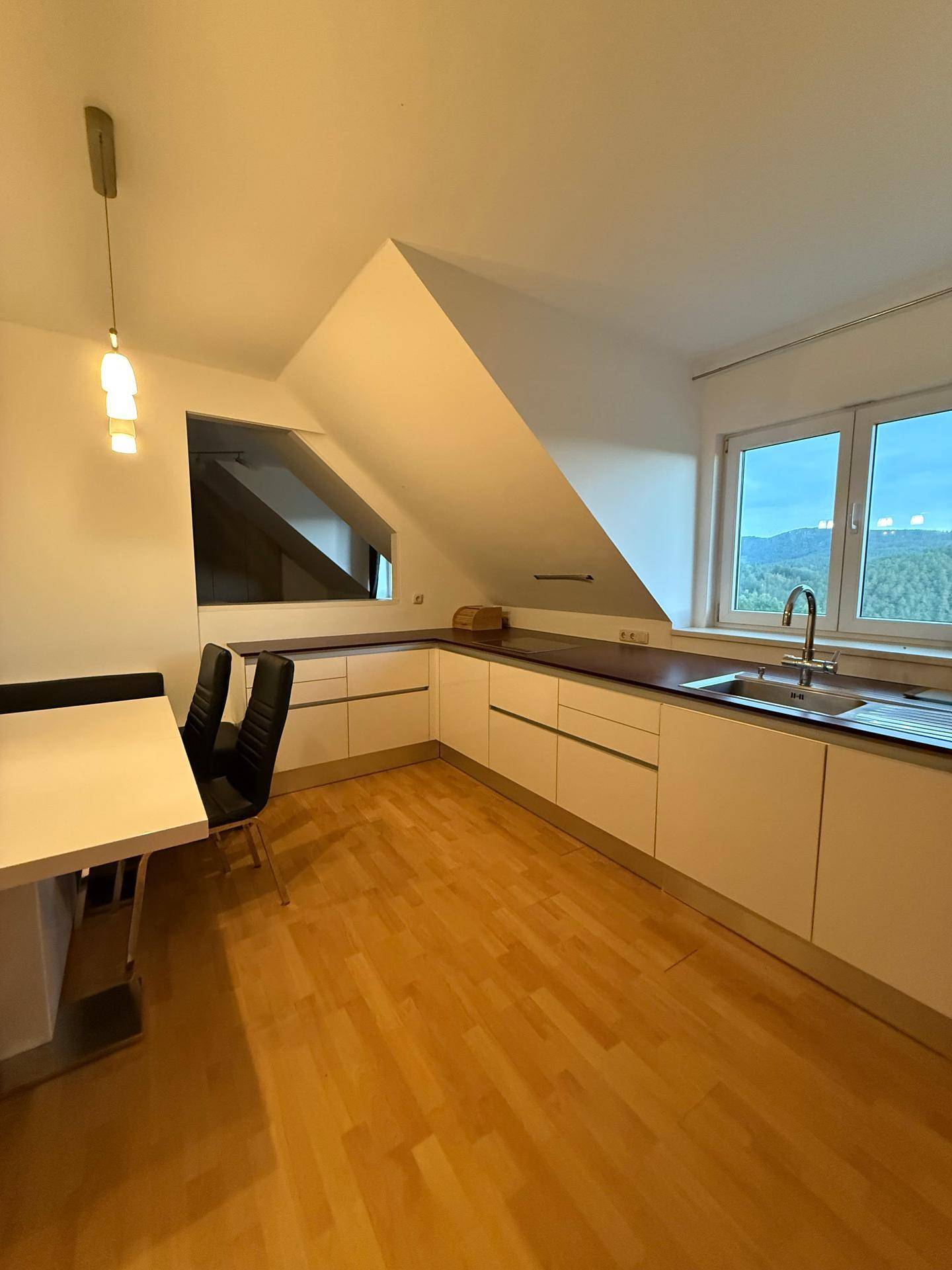 Moderne Küche im Dachgeschoss mit weißen Schränken, Holzboden und Essbereich unter der Dachschräge.