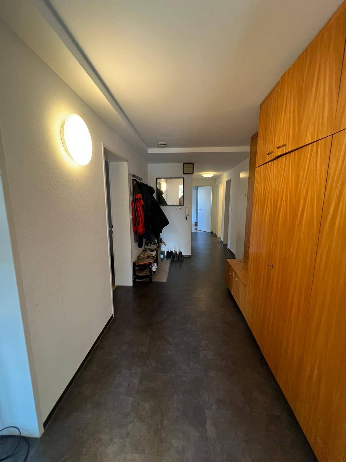 Langer Flur mit dunklem Boden, integrierten Holzschränken und Garderobe für zusätzlichen Stauraum.