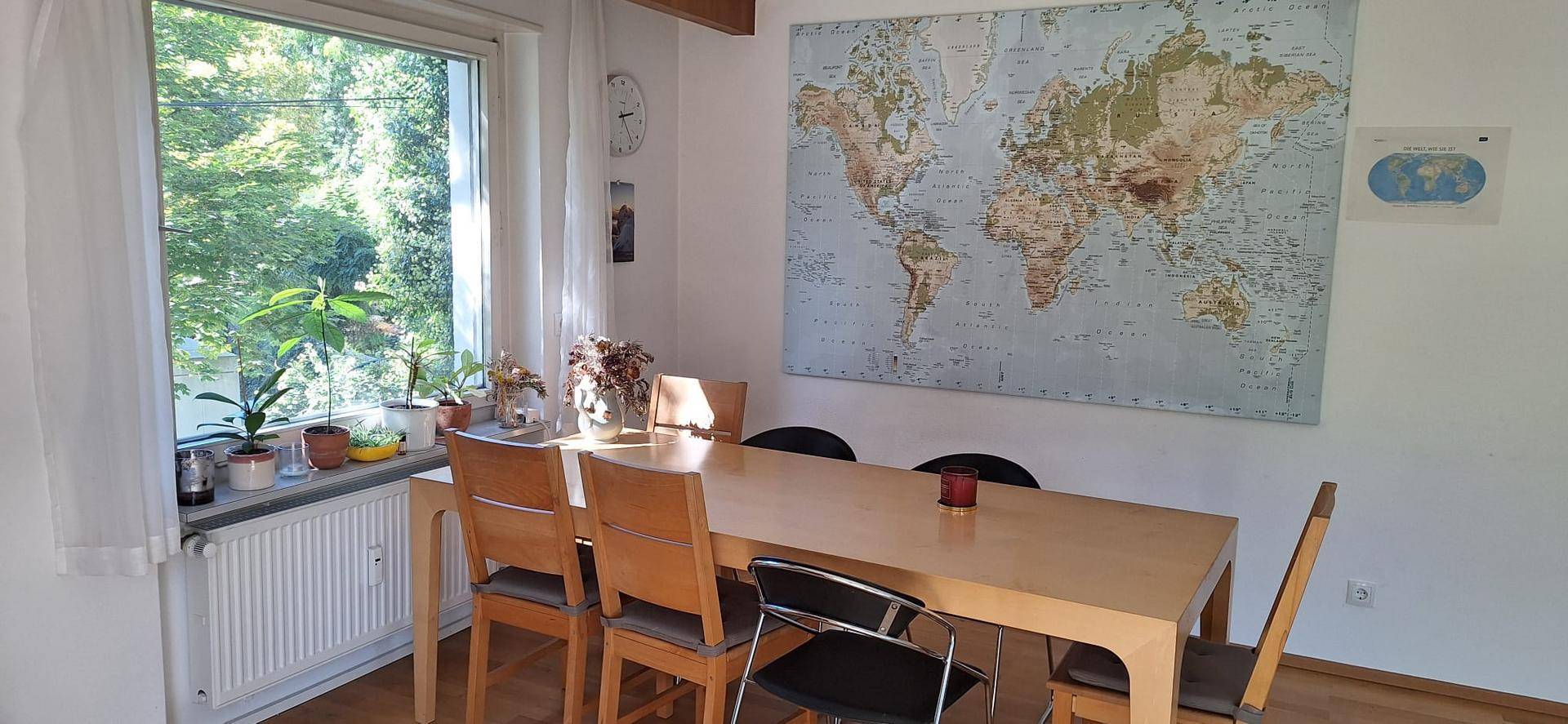 Gemütlicher Essbereich mit Holztisch, Stühlen und einem großen Fenster mit Blick ins Grüne.