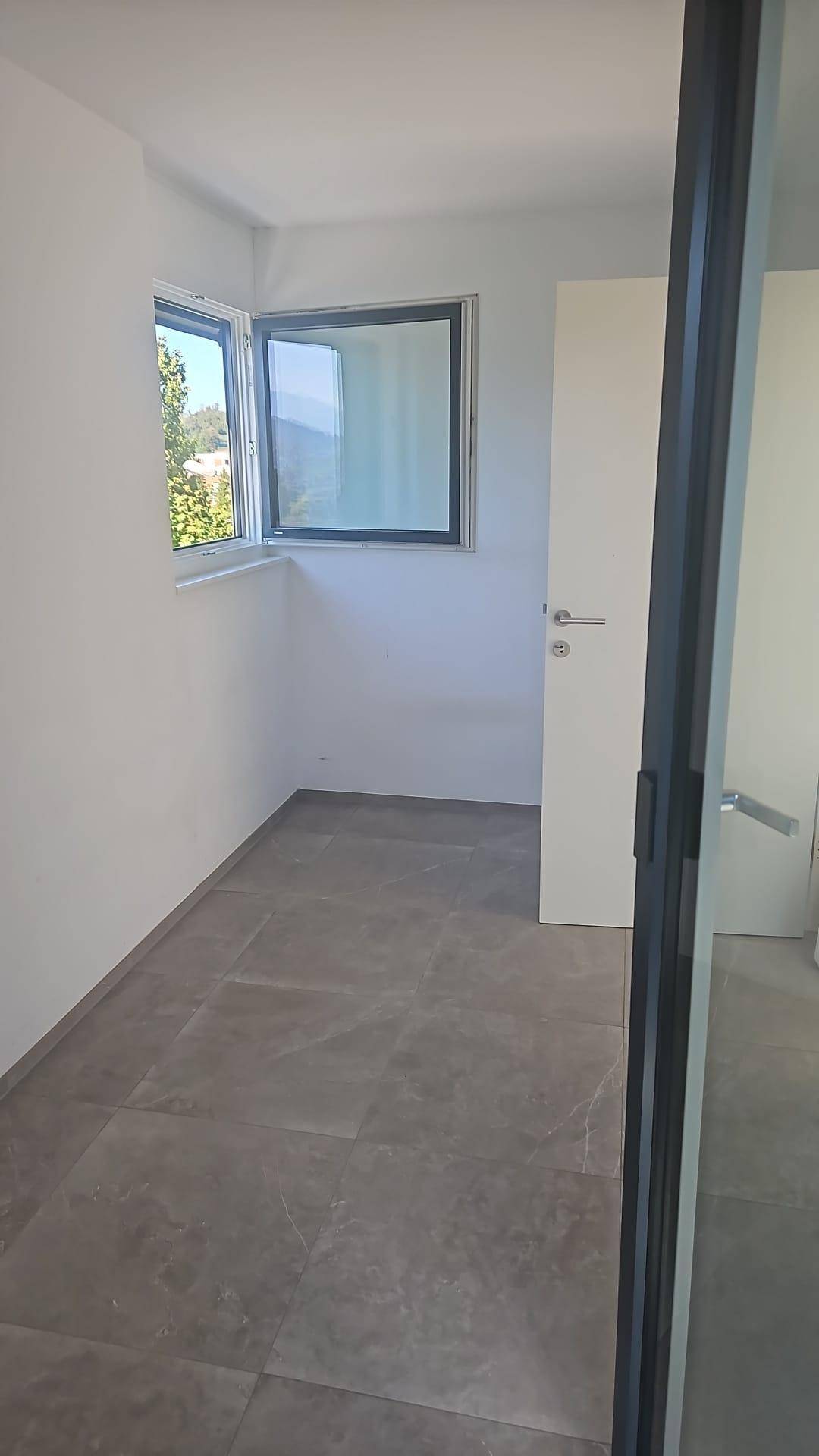 Heller, leerer Raum mit grauen Fliesen und einem Fenster, bereit zur individuellen Gestaltung.